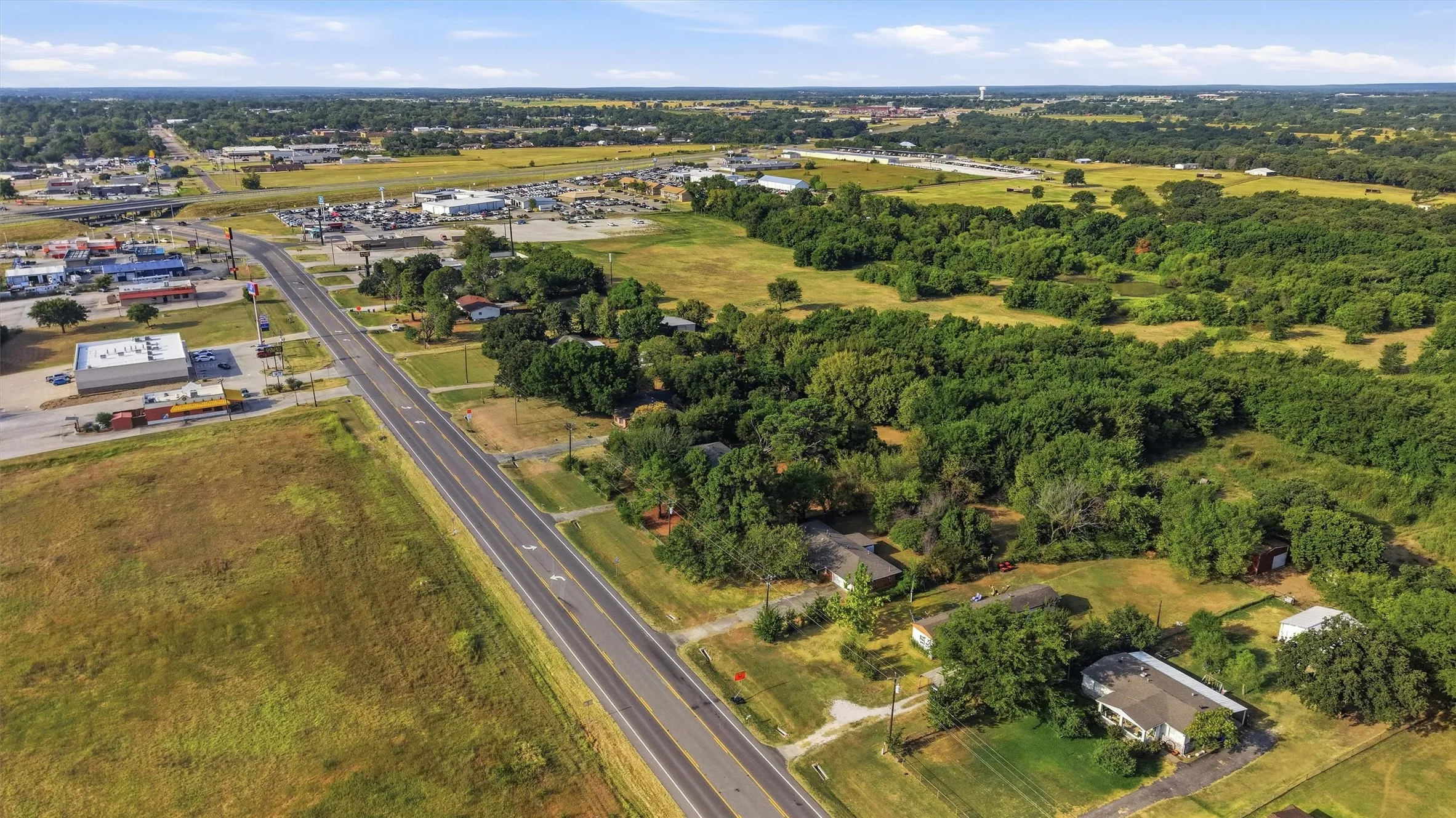 Expansive aerial perspective featuring a multi-lane roadway, surrounding commercial structures, and verdant tree coverage