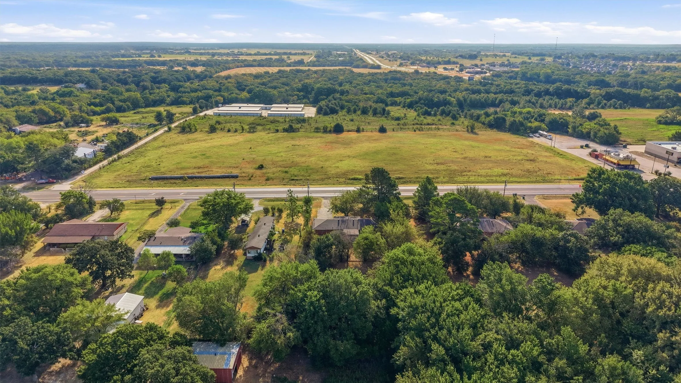 Expansive rural landscape featuring a large undeveloped parcel, surrounding mature trees, and visible roadways