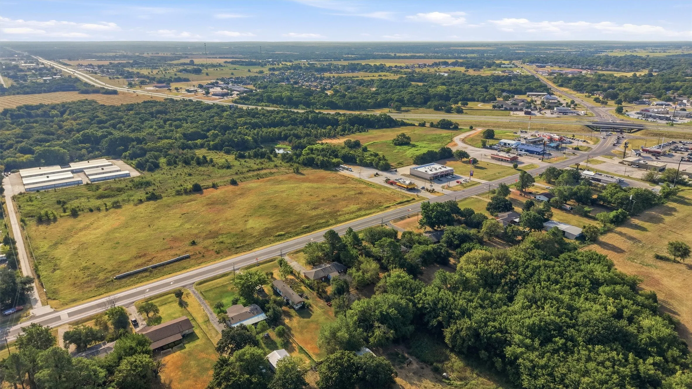 Expansive undeveloped land featuring a clear parcel, surrounding wooded areas, and proximity to established roadways and commercial structures