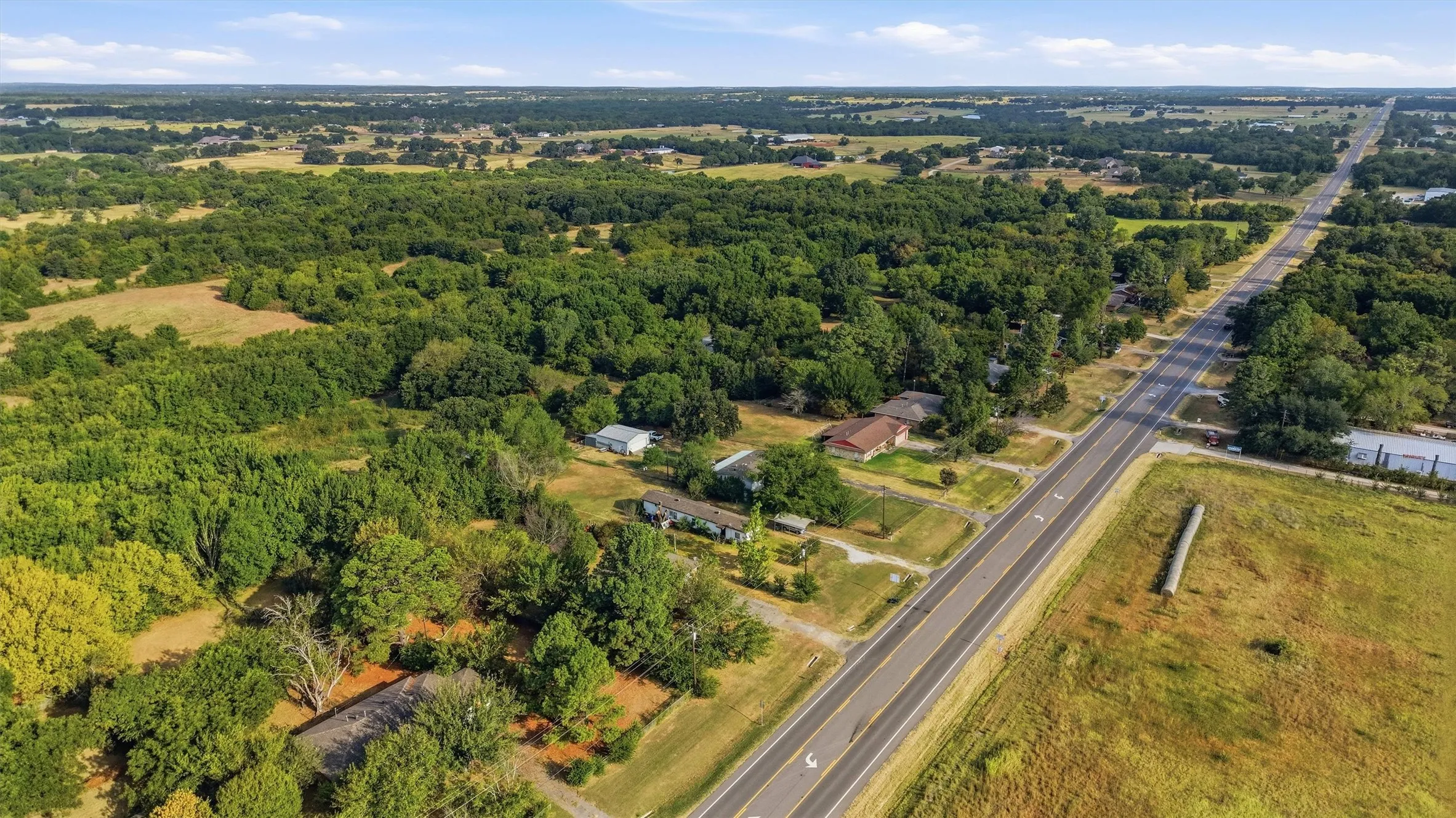 Expansive rural landscape featuring a paved roadway, mature trees, and open fields