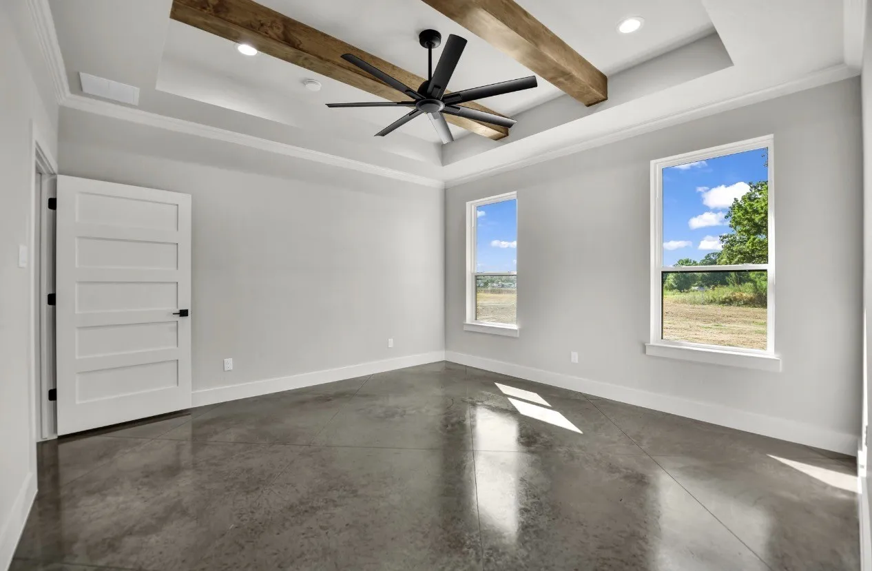 Tray ceiling with exposed wood beams, ceiling fan, polished concrete flooring, white trim, and two pane windows
