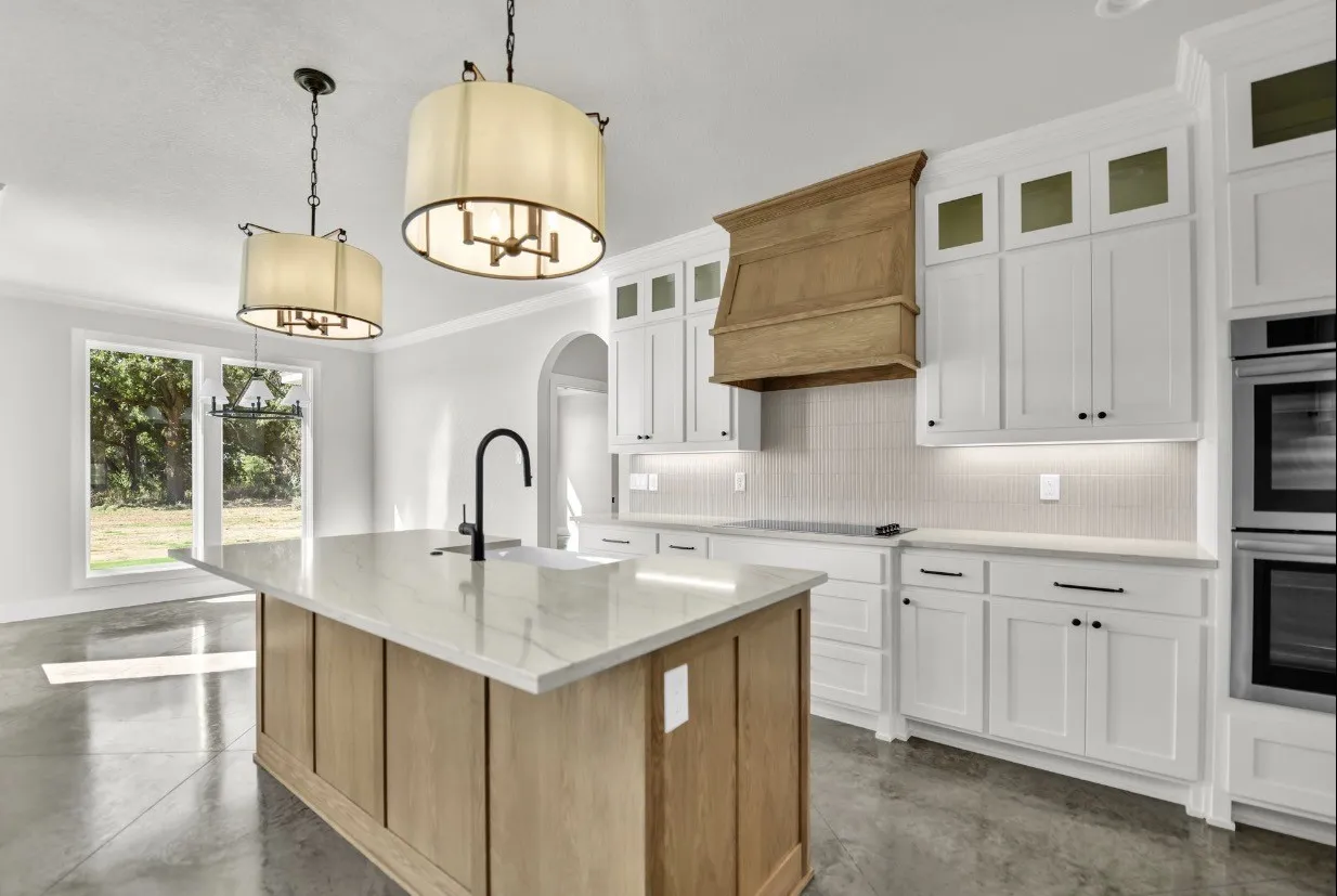 Kitchen featuring an island with stone countertops, a built-in sink with a gooseneck faucet, white shaker-style cabinetry, and a wood-finish range hood