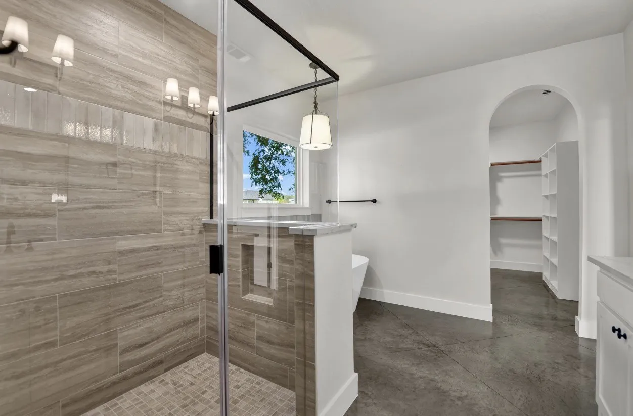 Glass-enclosed shower with tile surround and mosaic floor, freestanding bathtub, arched doorway, and built-in closet shelving