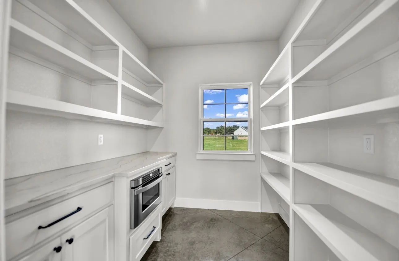 Built-in shelving, countertop space, integrated microwave, white cabinetry, and a window