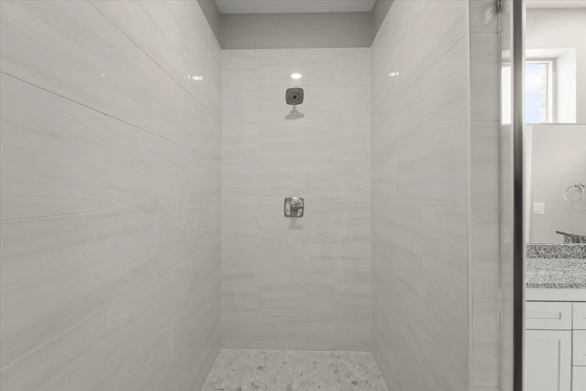 Walk-in shower with light-toned wall tile, pebble floor tile, and chrome fixtures