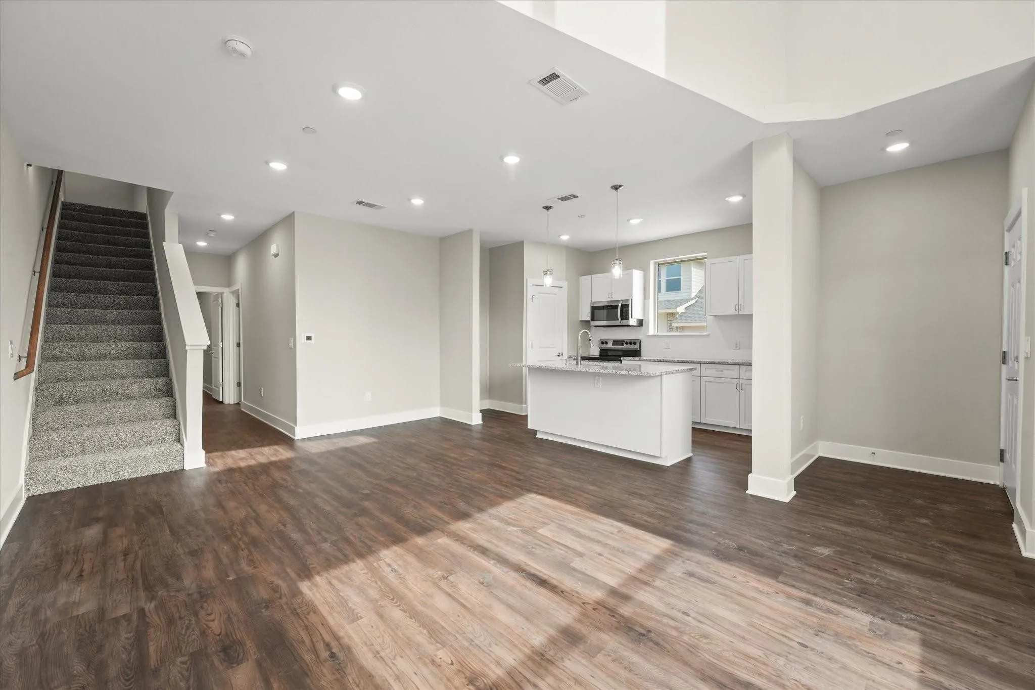 Open-concept living space featuring wood-finish flooring, recessed lighting, a kitchen island, and a staircase with carpeted treads