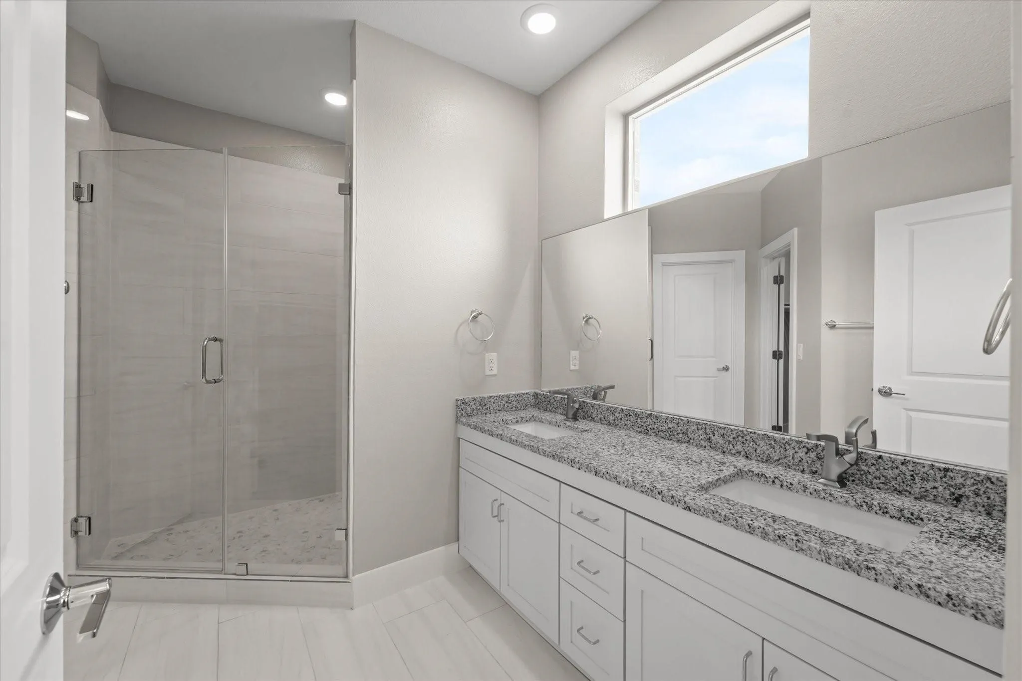 Dual vanity with stone countertop, frameless glass shower enclosure, and transom window
