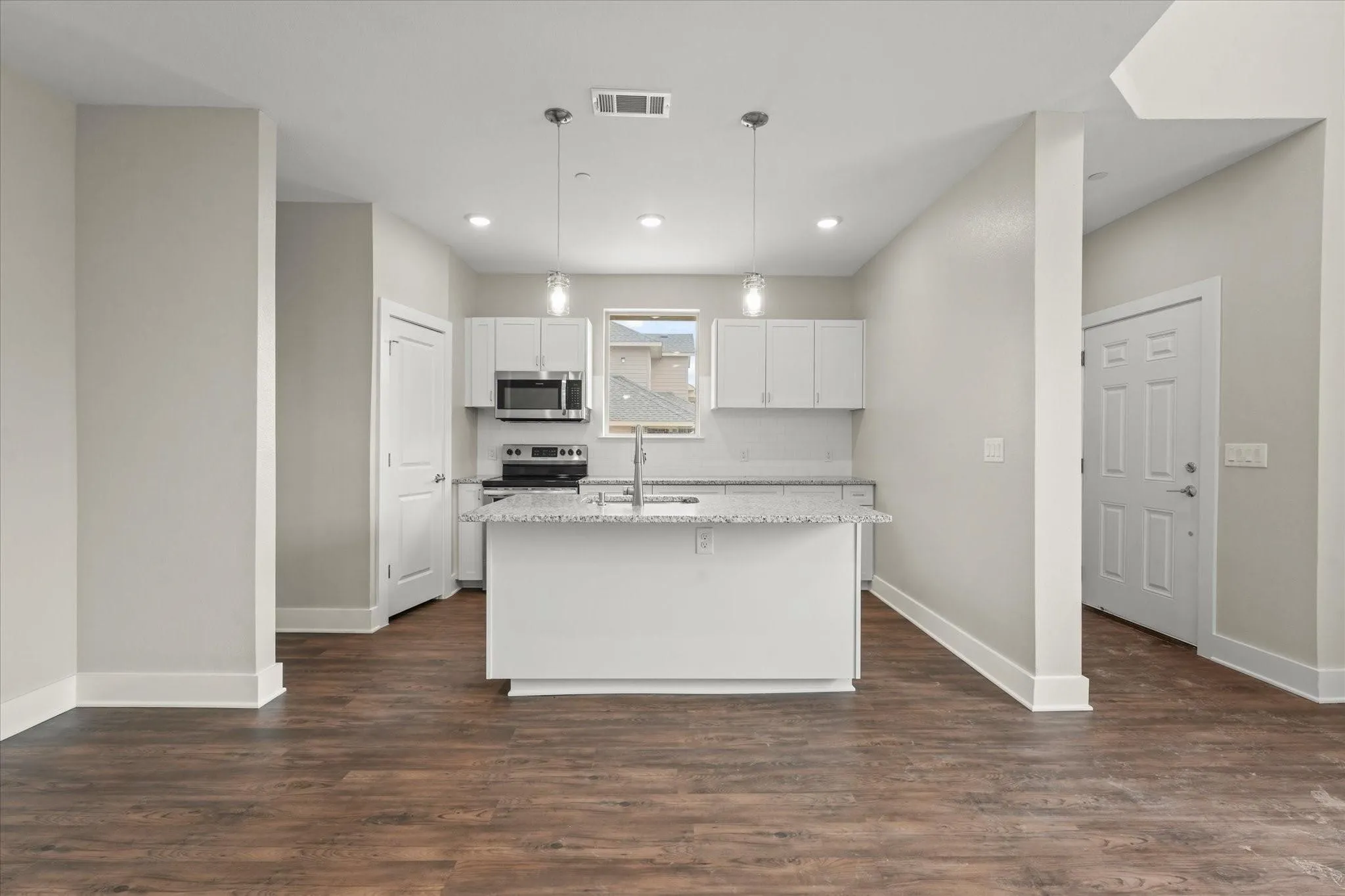 Kitchen island with granite countertop, stainless steel appliances, white cabinetry, subway tile backsplash, and wood-finish flooring