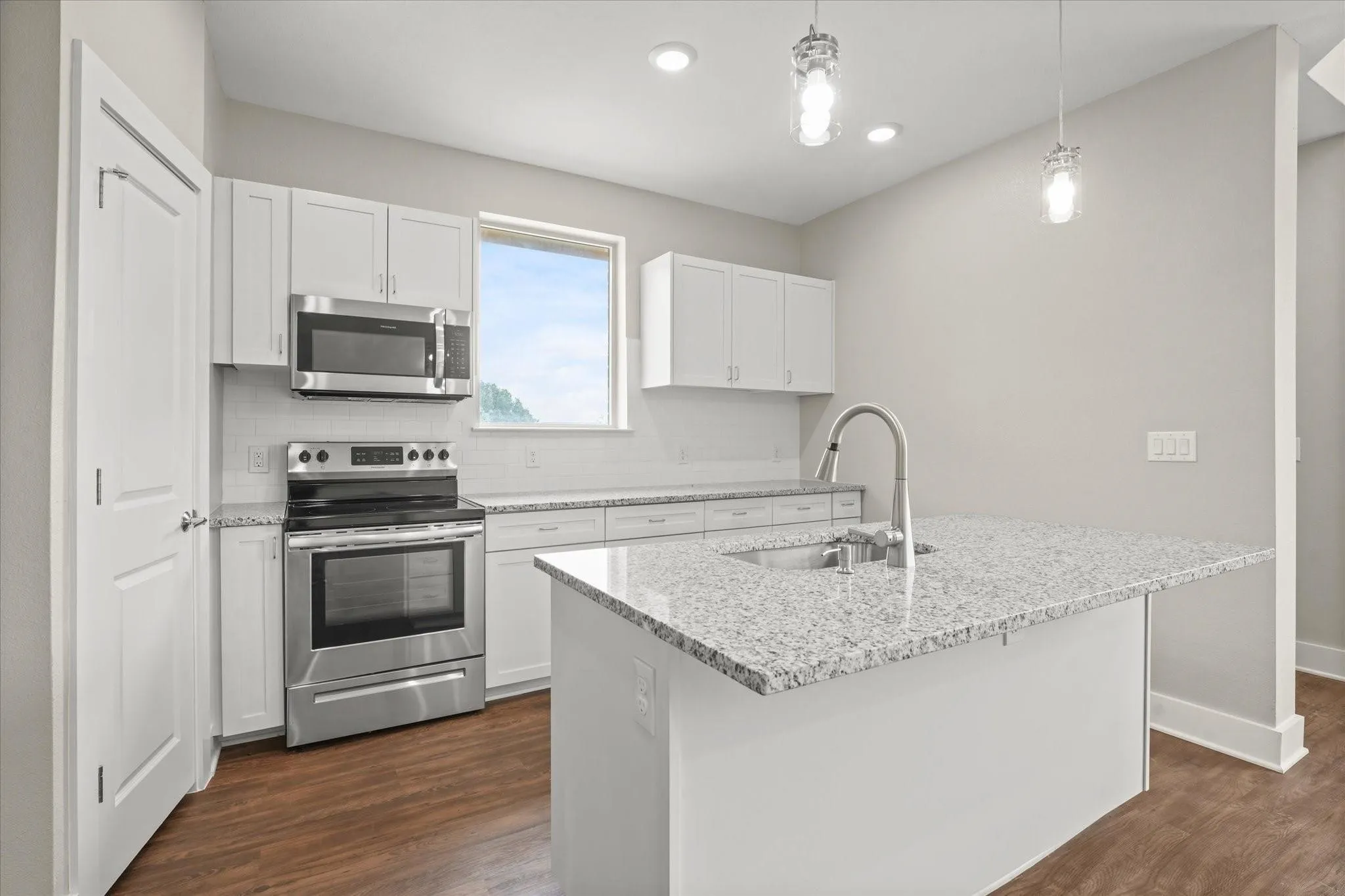 Kitchen featuring a center island with a stainless steel sink and granite countertop, white cabinetry, stainless steel appliances, and wood-finish flooring