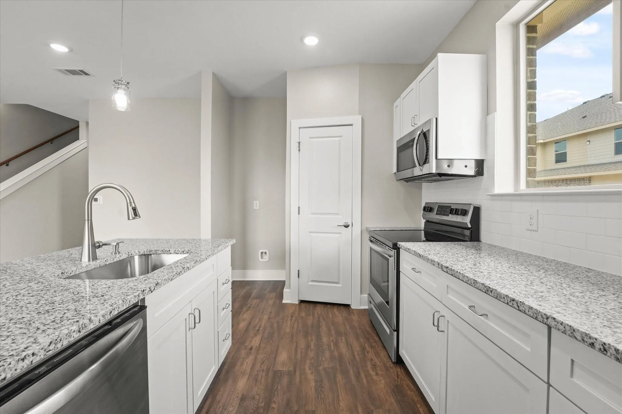 Modern kitchen featuring white cabinetry, light-toned granite countertops, stainless steel appliances, wood-finish flooring, and a subway tile backsplash