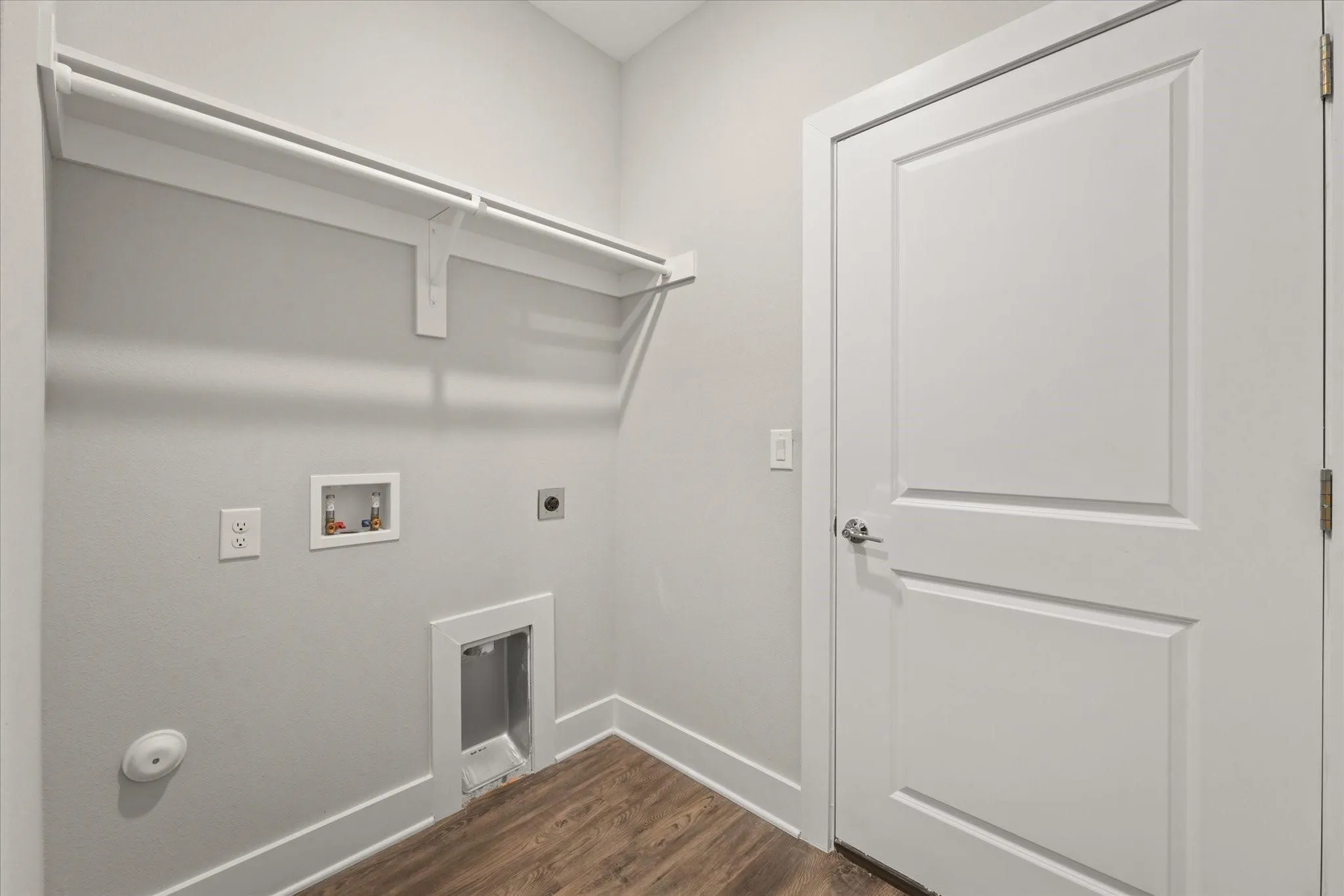 Laundry area featuring wood-finish flooring, white trim, and a built-in shelf with hanging rod
