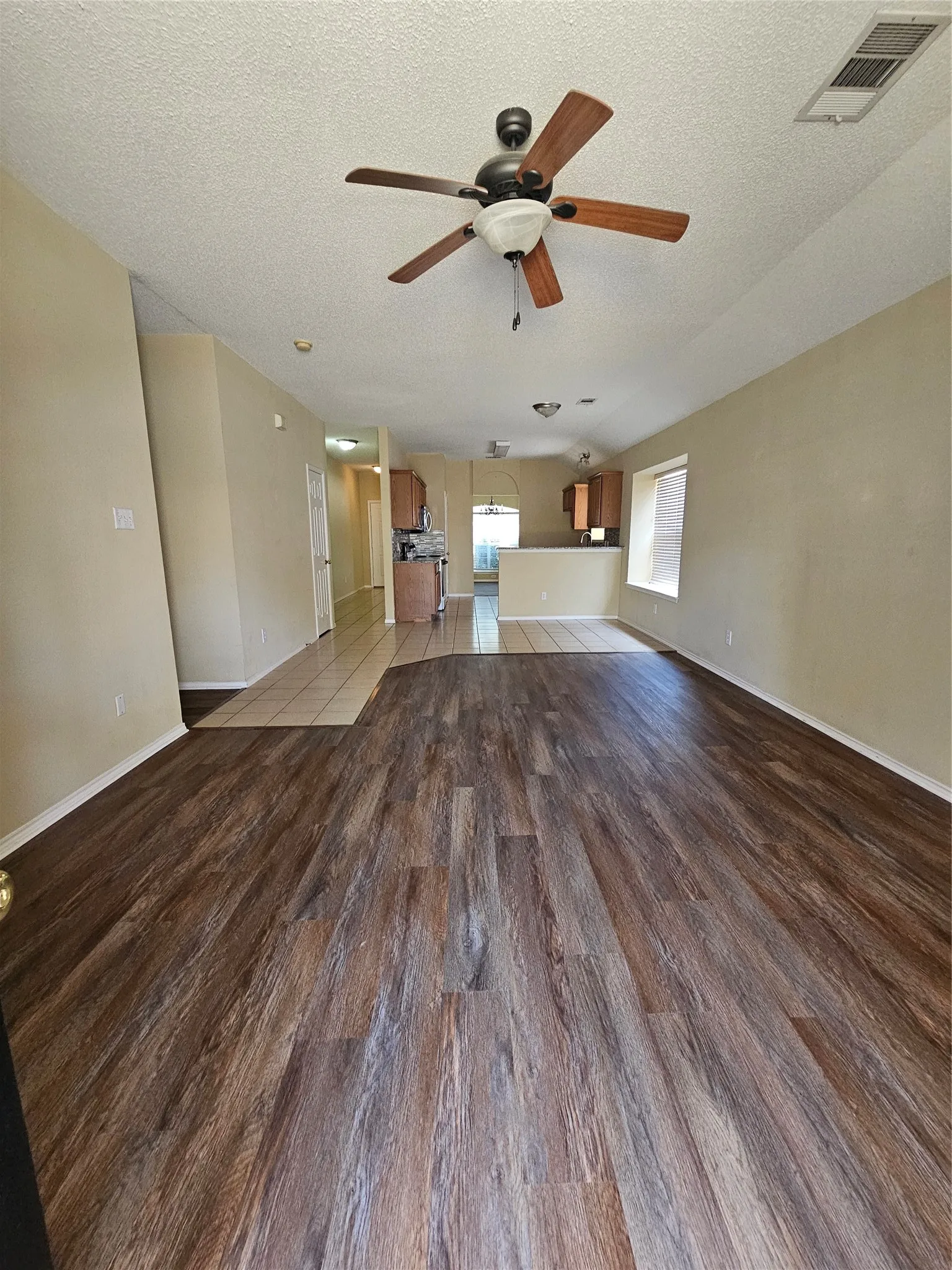 Expansive living area featuring wood-finish flooring, a ceiling fan with light fixture, and neutral wall tones
