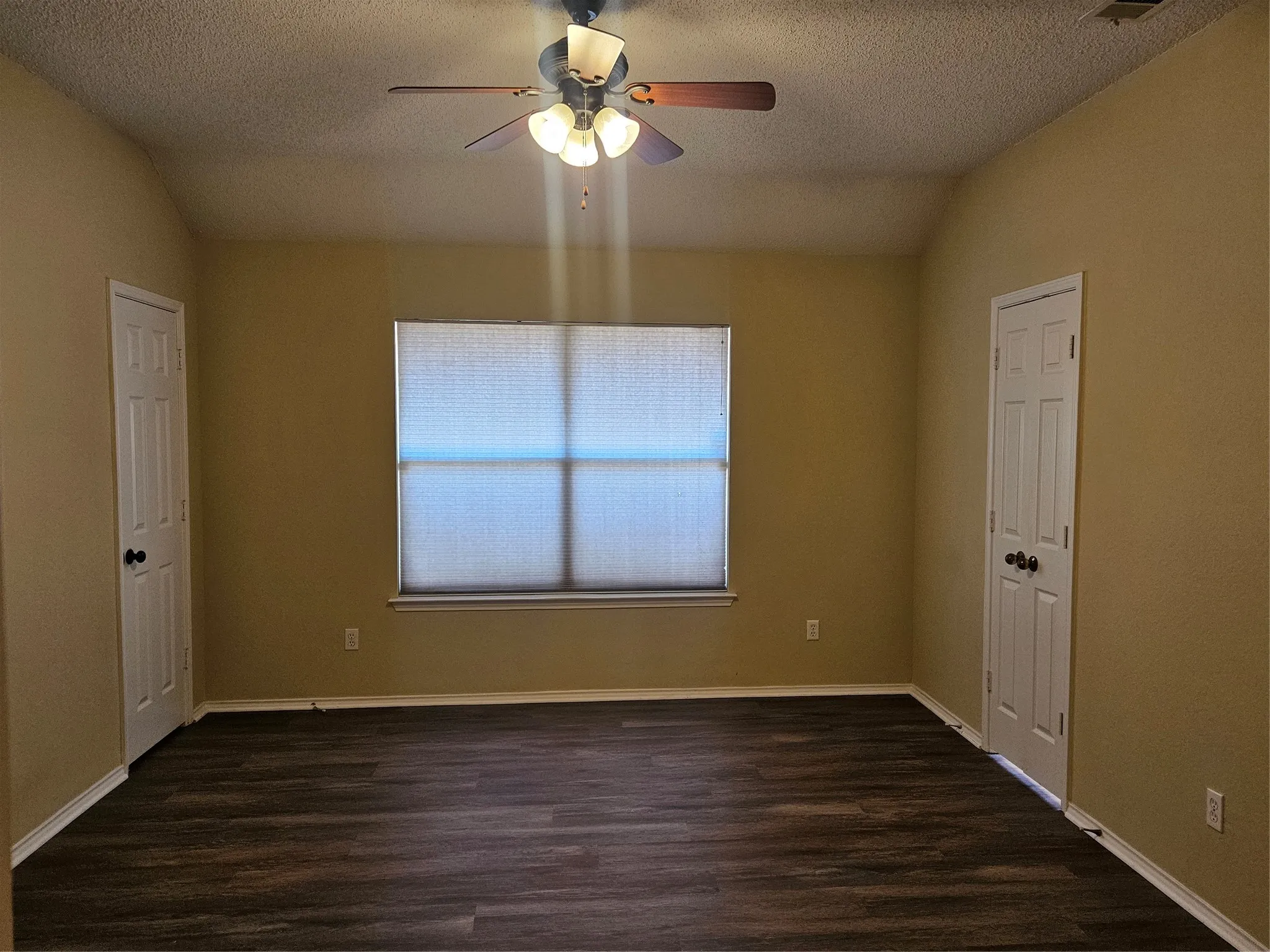 Vaulted ceiling, wood-finish flooring, ceiling fan with integrated lighting, window with blinds, and white paneled doors