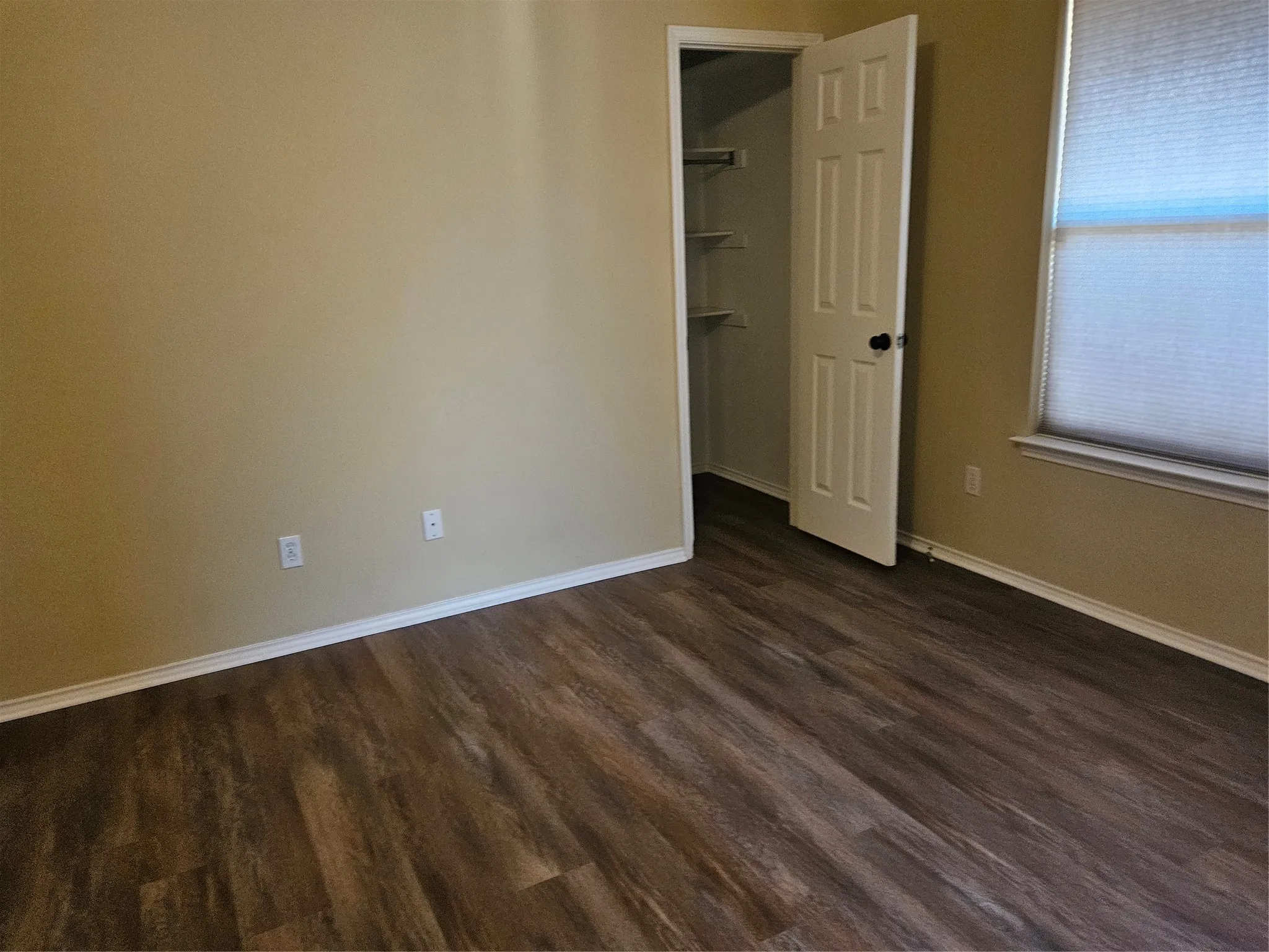 Wood-finish flooring throughout, neutral painted walls, white trim, and a window with blinds