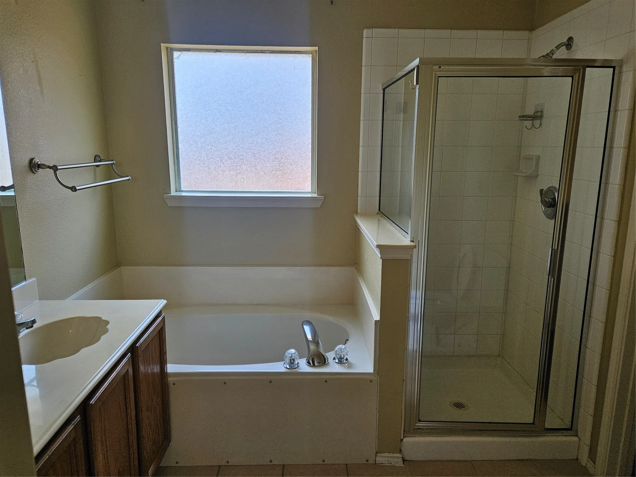 Bathroom featuring a built-in tub, separate glass-enclosed shower with tile surround, wood-finish vanity with an integrated sink, and a frosted window