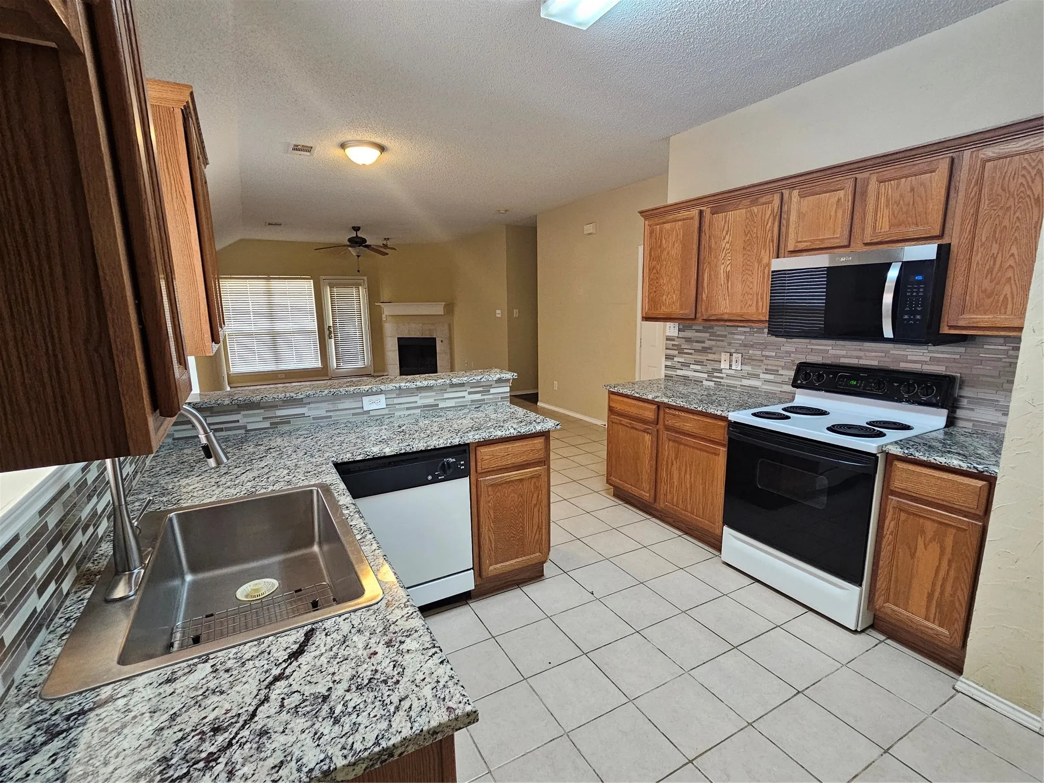 Kitchen featuring wood cabinetry, granite countertops, a stainless steel sink, and a tile backsplash
