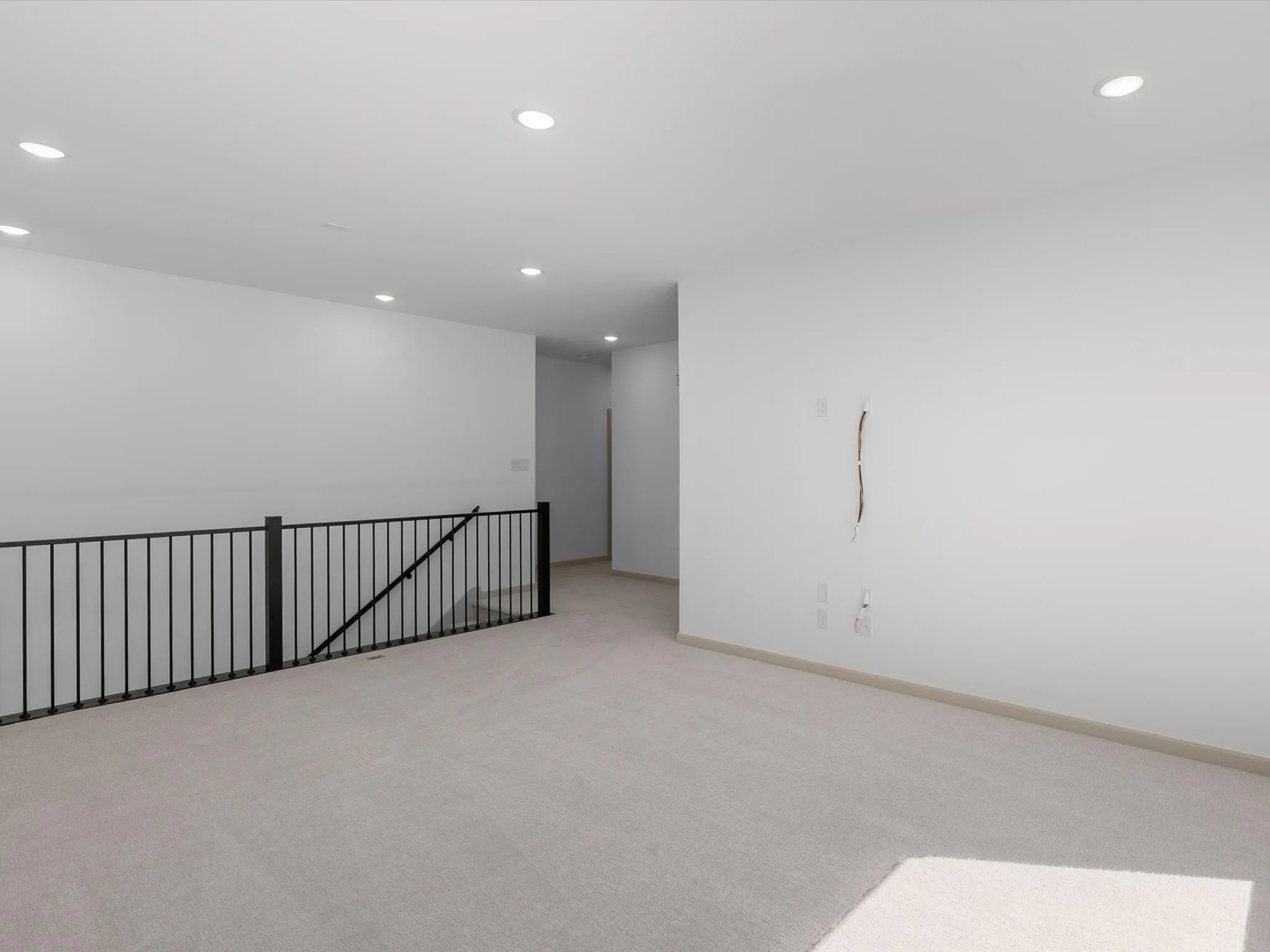 Carpeted loft area with recessed lighting and a black metal railing