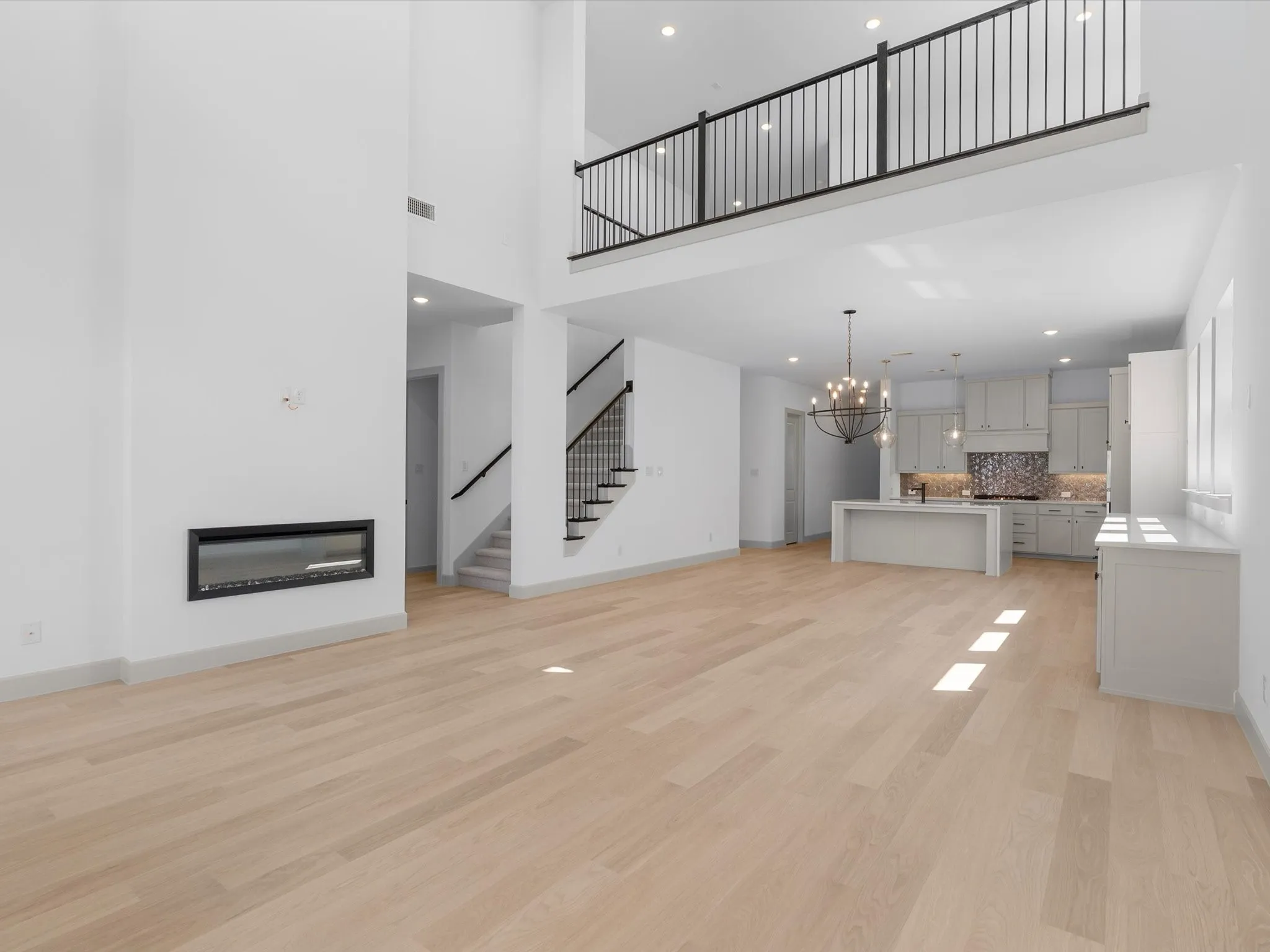 Living Room featuring Soaring ceilings with recessed lighting, linear electric fireplace, wood-finish flooring, open kitchen with island seating, and a second-story balcony with metal railings