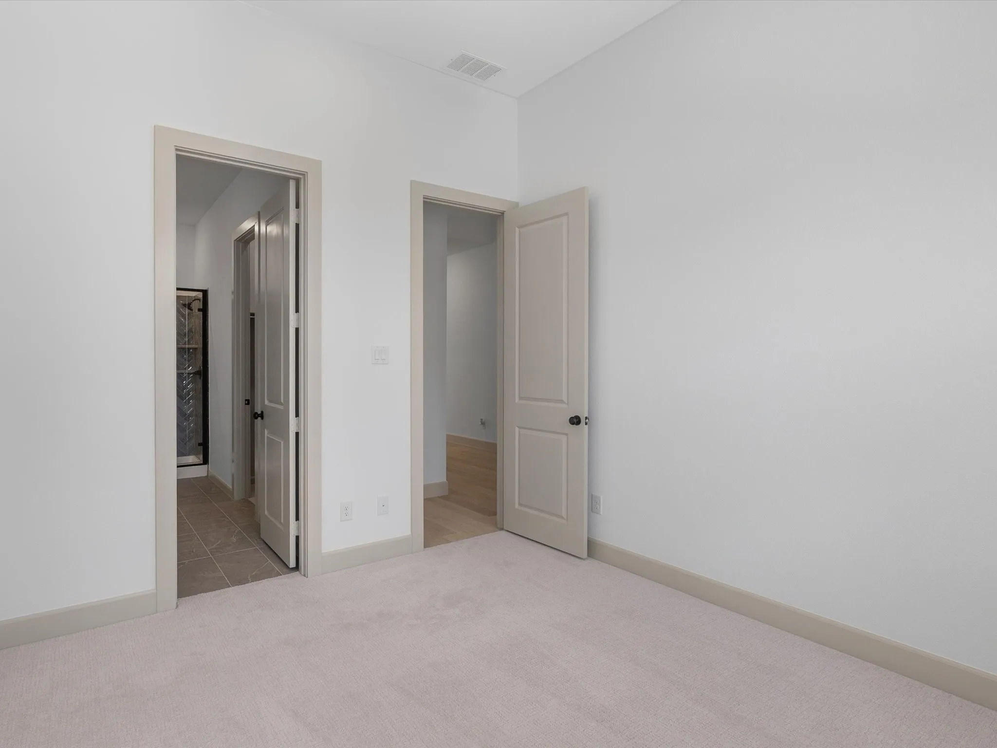 Downstairs 2nd Bedroom with ensuite bathroom and Neutral tone wall color, carpeted flooring, two interior doorways, and light-colored trim throughout