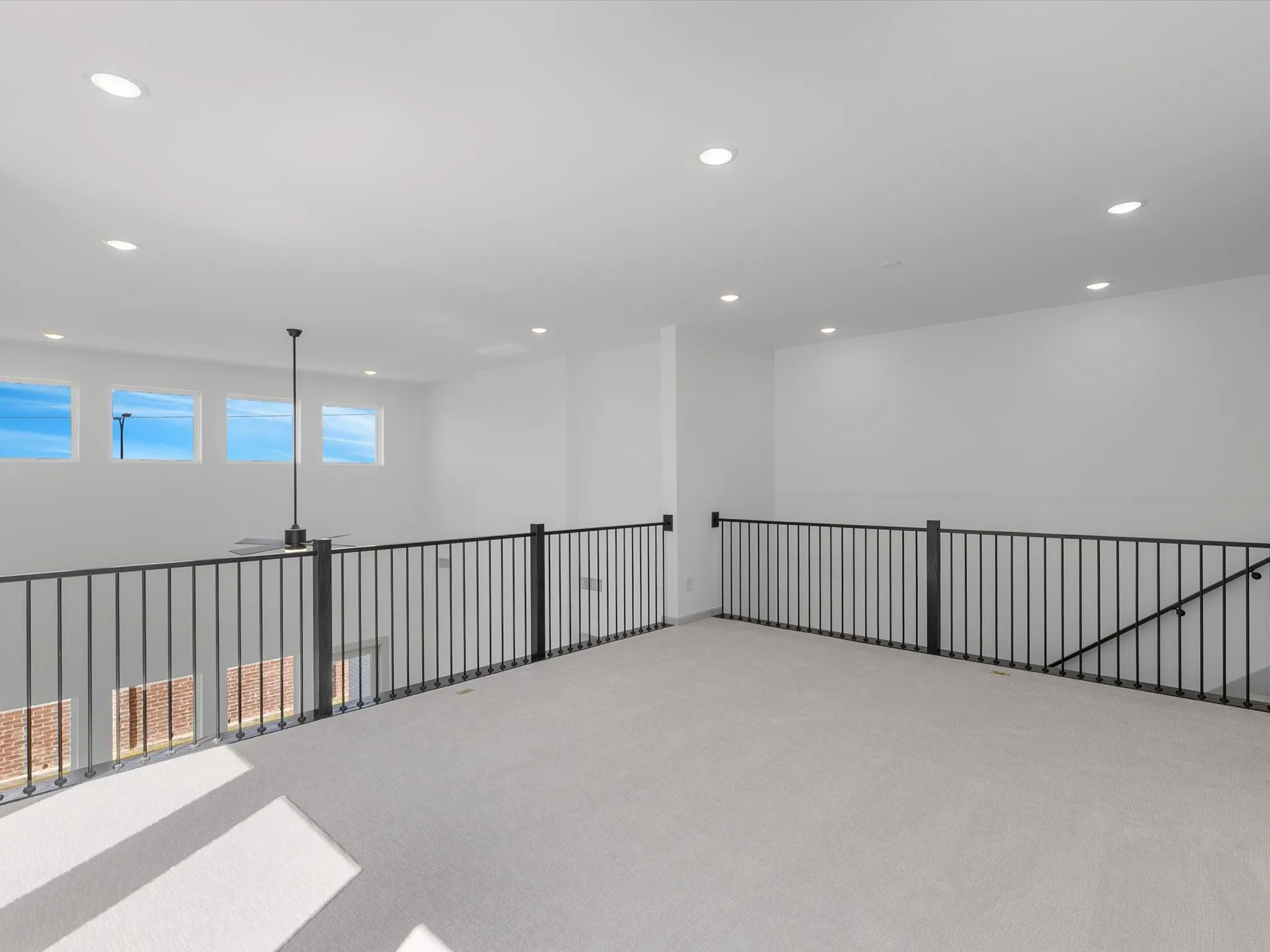 Expansive loft area with light-colored carpeting, recessed lighting, and a modern ceiling fan