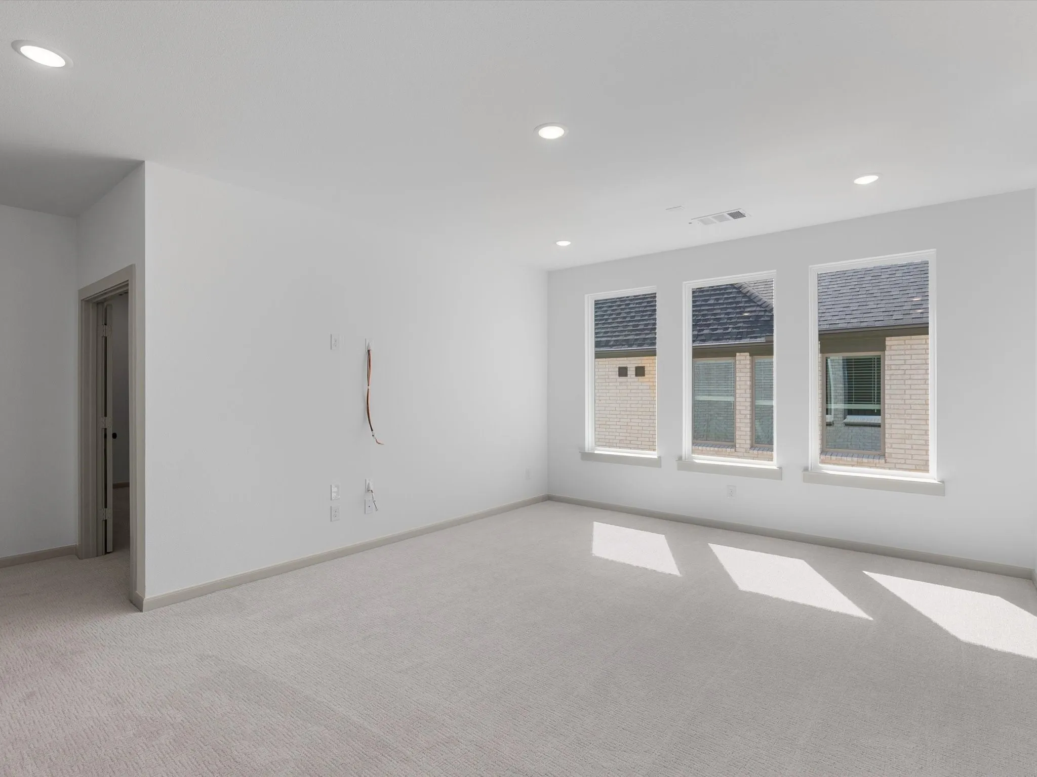 Neutral tone carpeting, recessed ceiling lighting, three windows with white frames, and a paneled interior door
