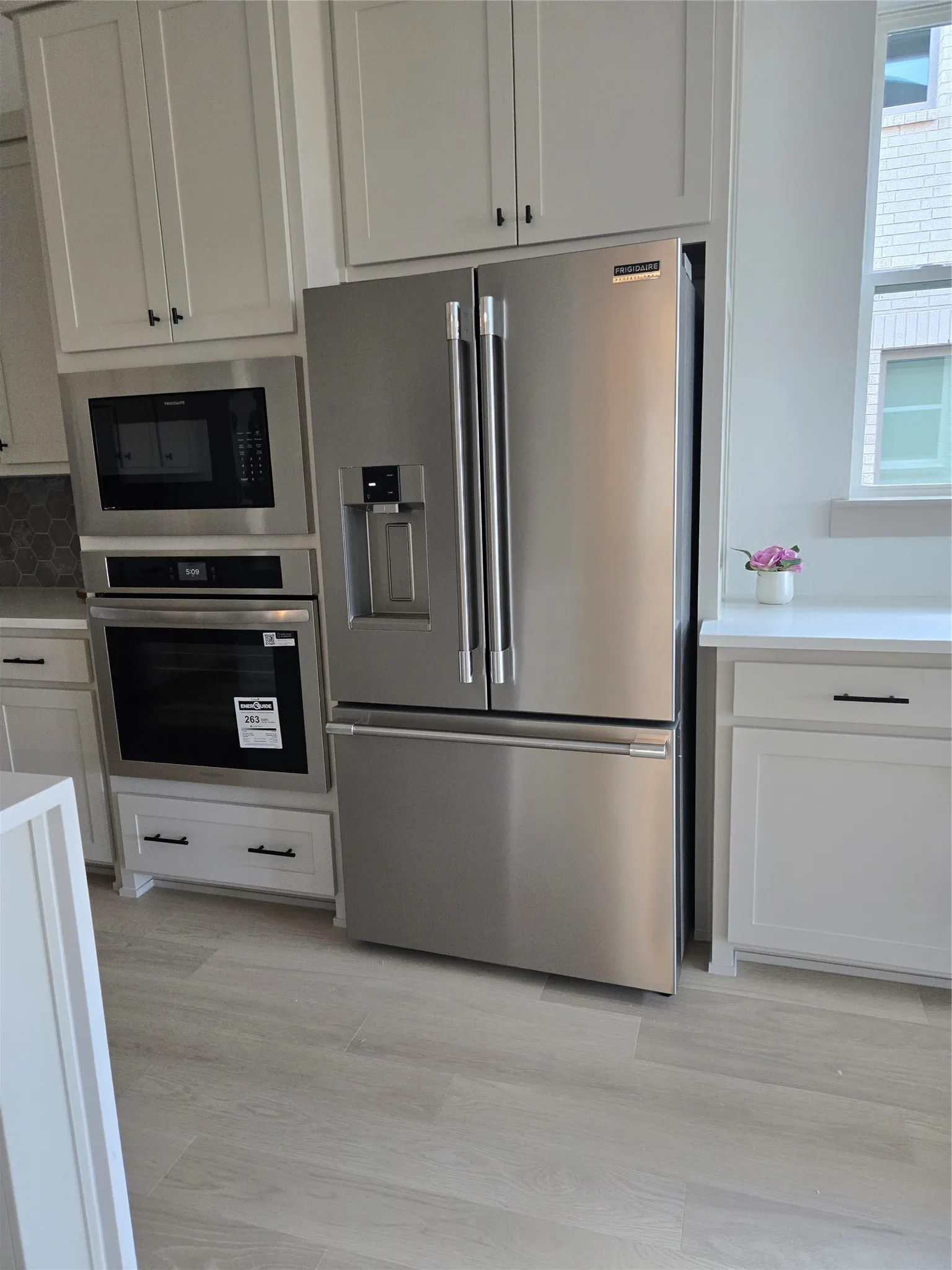 Stainless steel French door refrigerator, built-in microwave, built-in oven, white shaker cabinetry, and light wood-finish flooring