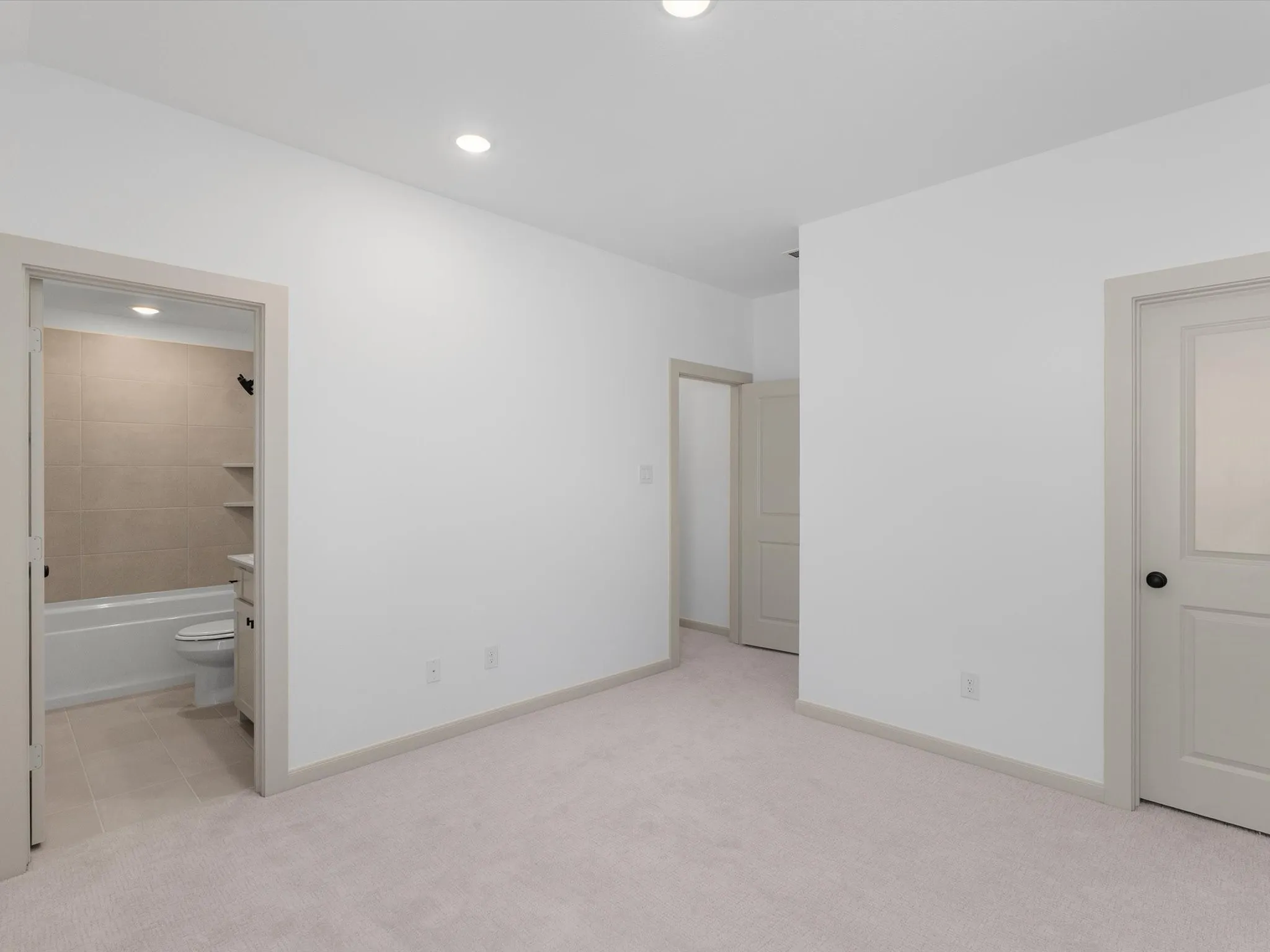 Bedroom 1 of 3 upstairs - Recessed ceiling lighting, light-toned carpeting, neutral wall paint, and a bathroom with a tiled shower surround and built-in shelving