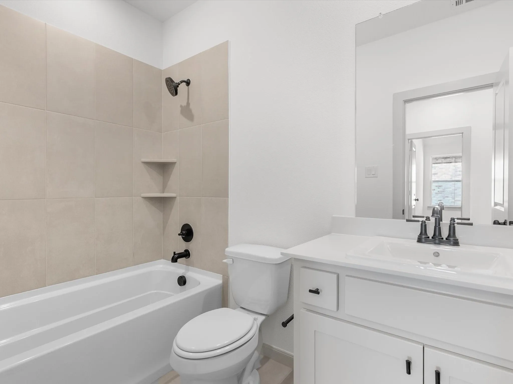Bathroom featuring a white bathtub, tiled shower surround with built-in shelving, white vanity with an integrated sink, and black fixtures