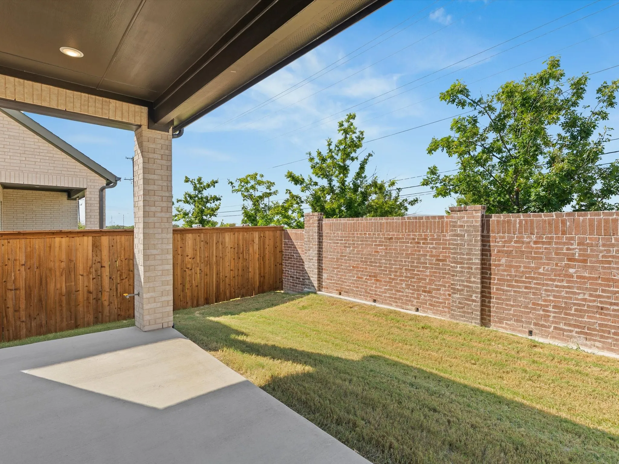 Covered patio with a concrete surface, a manicured lawn, a wood fence, and a brick wall