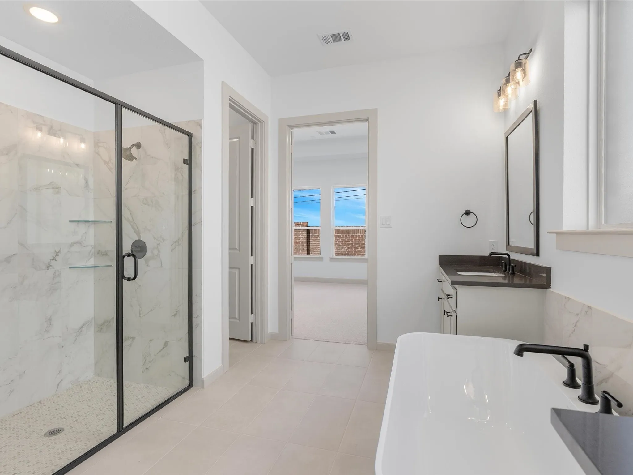 Spacious bathroom featuring a frameless glass shower enclosure with marble-finish tile, an elongated soaking tub with matte black fixtures, a floating vanity with a vessel sink, and large format floor tiling
