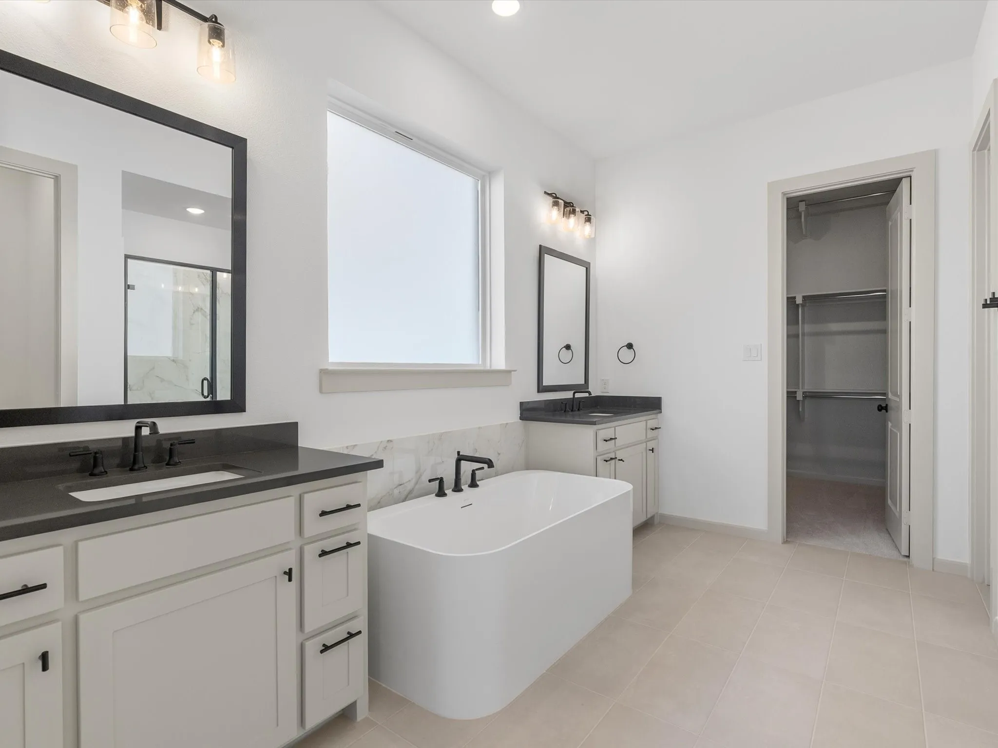 Primary Bath - Dual vanities with dark countertops, a freestanding soaking tub, and a window for natural illumination