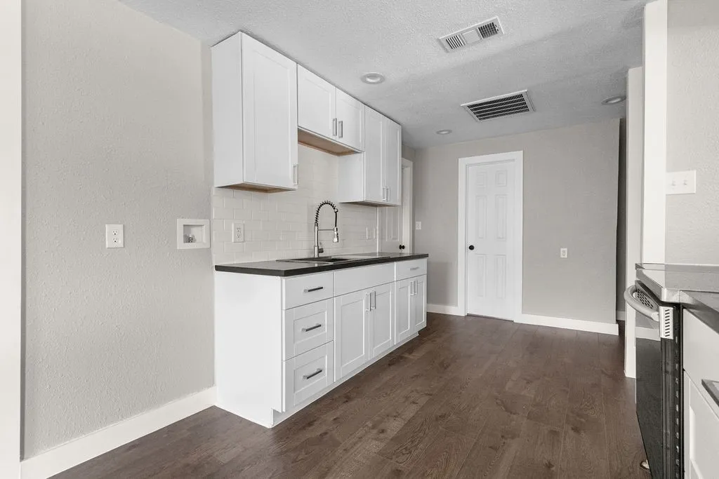 White cabinetry with brushed nickel hardware, dark countertops, a subway tile backsplash, stainless steel sink, and wood-finish flooring