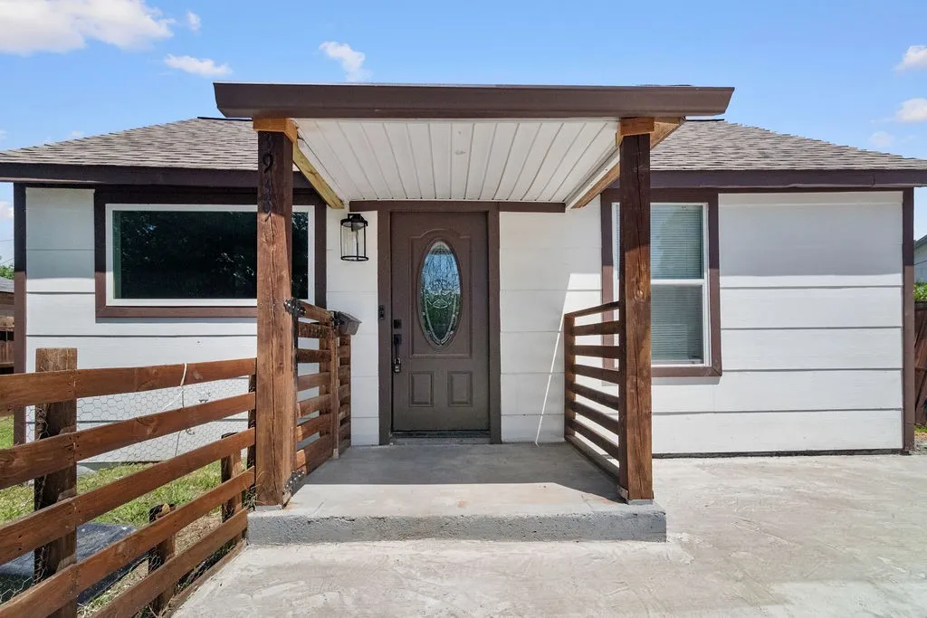 Front entry with a covered porch, wood-finish railing, and sconce lighting
