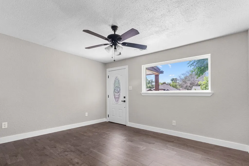 Wood-finish flooring, white trim, ceiling fan with integrated lighting, and a window with white casing