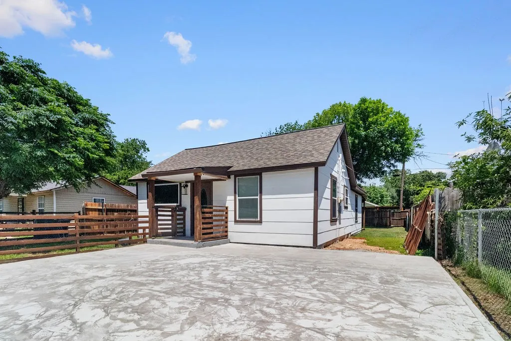 Exterior featuring white siding, dark trim, a covered front entry, a concrete parking pad, and a wood privacy fence