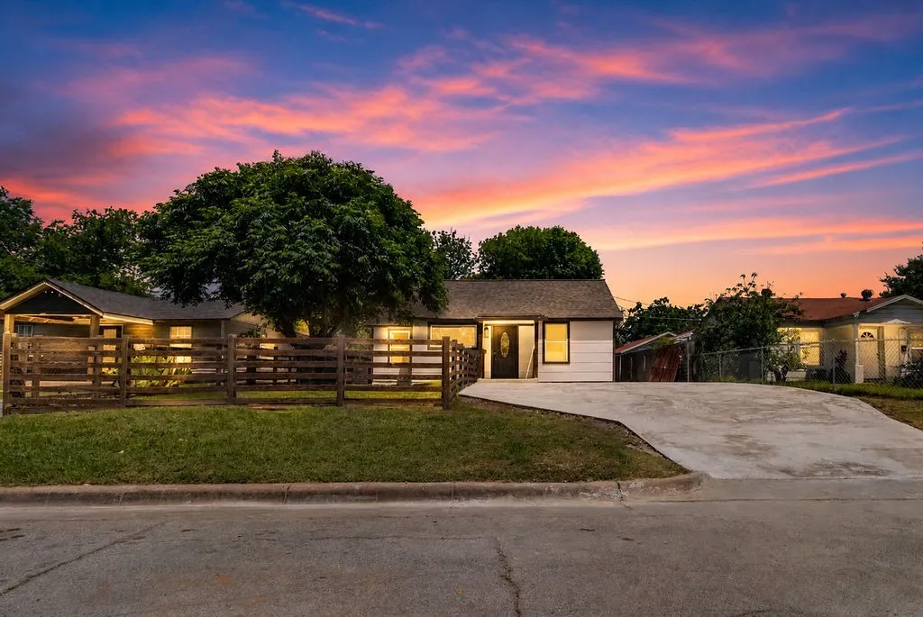 Single-story residence featuring a prominent mature tree, a split-rail fence, and a concrete driveway