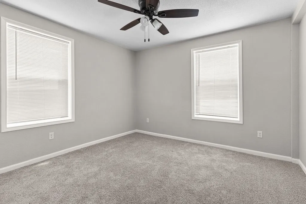 Soft gray carpet flooring, two windows with blinds, a ceiling fan, and light gray wall paint