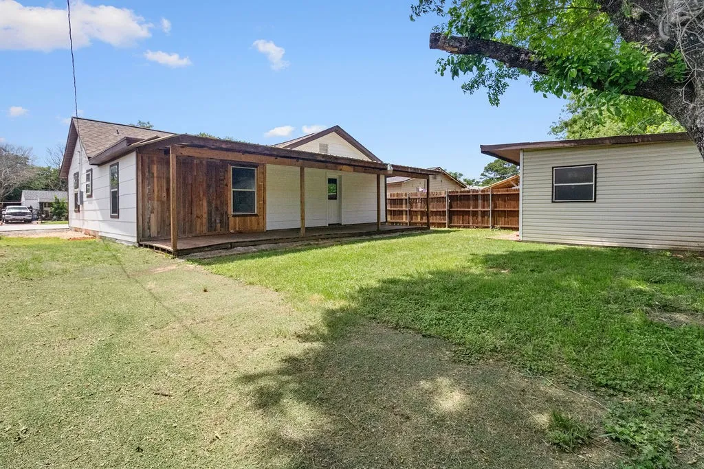 Expansive green space featuring a covered porch with wood-clad siding, a separate detached structure, and a wood privacy fence