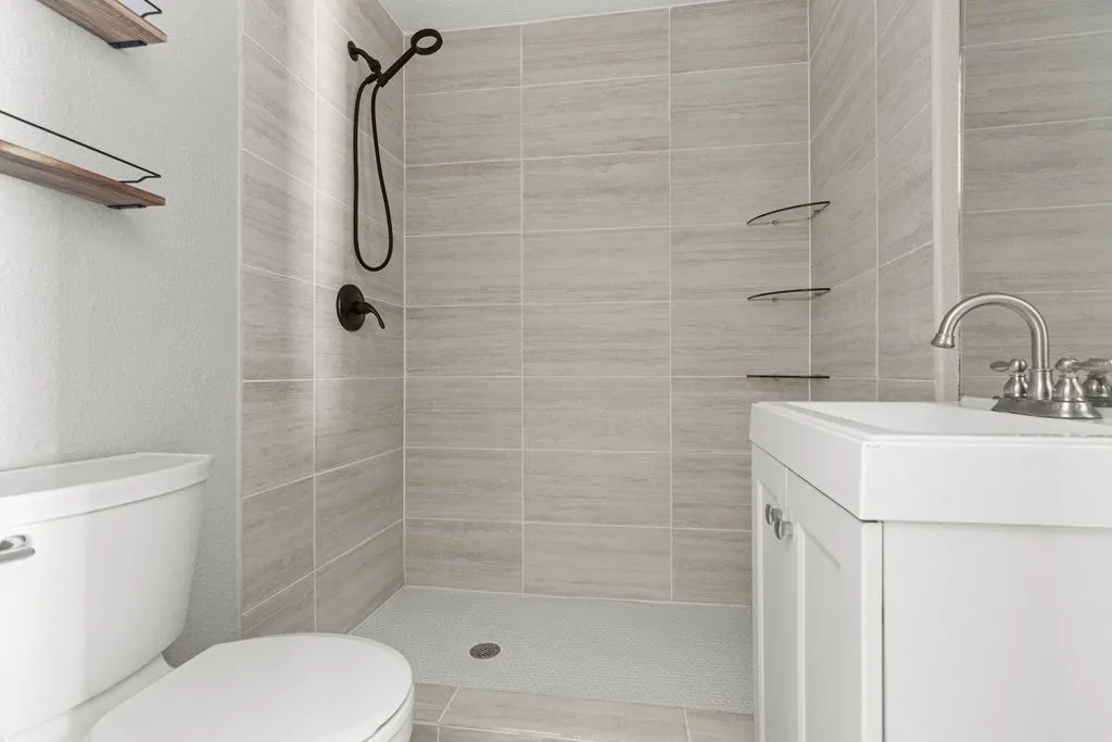 Shower stall with light-toned wall tile, white vanity with integrated sink, and brushed nickel faucet