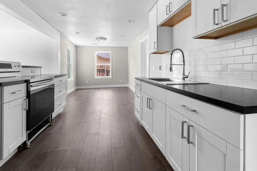 Kitchen featuring dark counters, white shaker-style cabinetry, a subway tile backsplash, stainless steel appliances, and wood-finish flooring