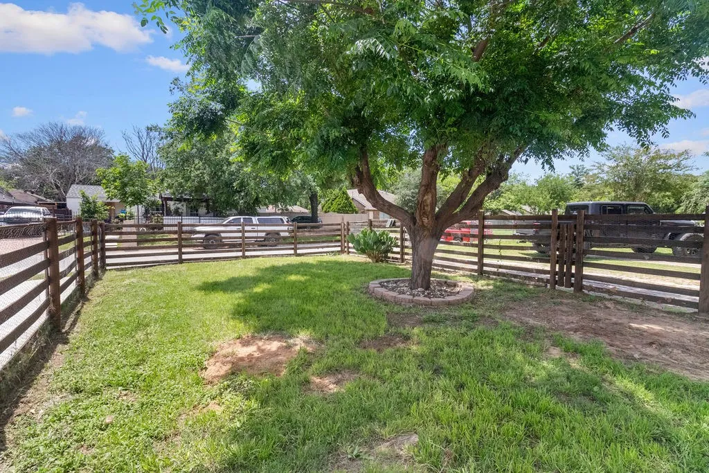 Fenced property featuring a mature tree with a stone-edged planter, and a partially graded ground surface