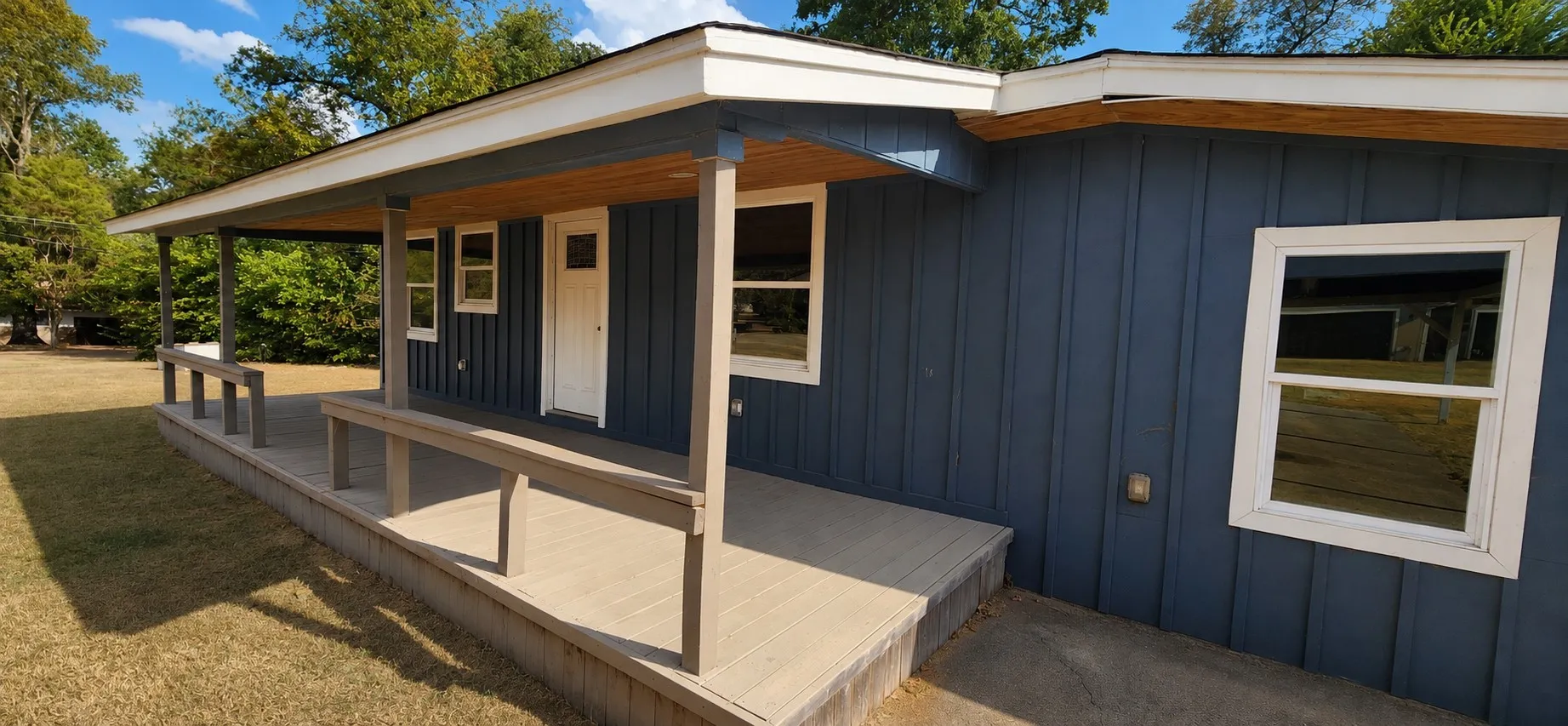 Exterior featuring dark blue vertical siding, white trim, a covered porch with composite decking, and white-framed windows