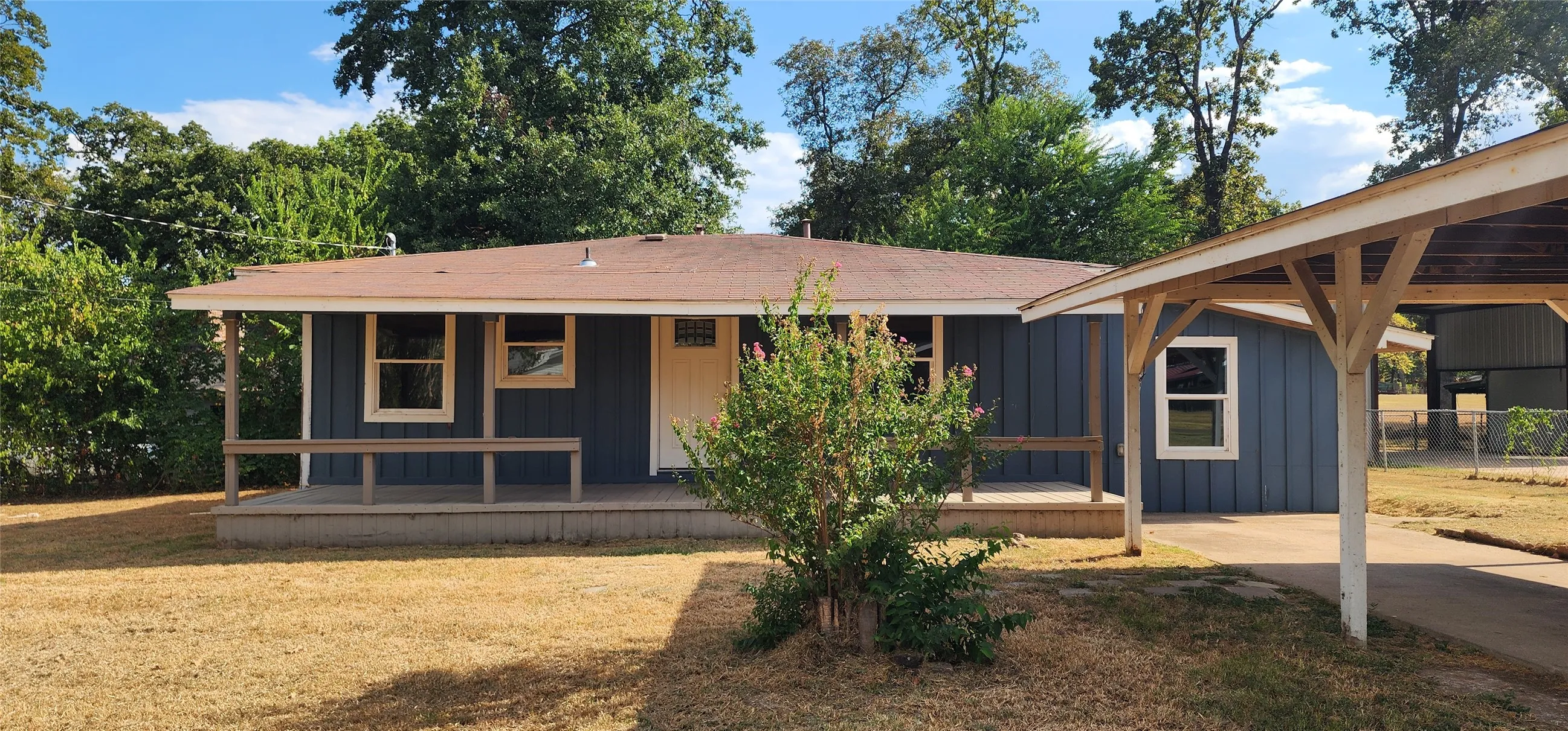 Blue siding exterior with a covered front porch, white-trimmed windows, and an attached carport