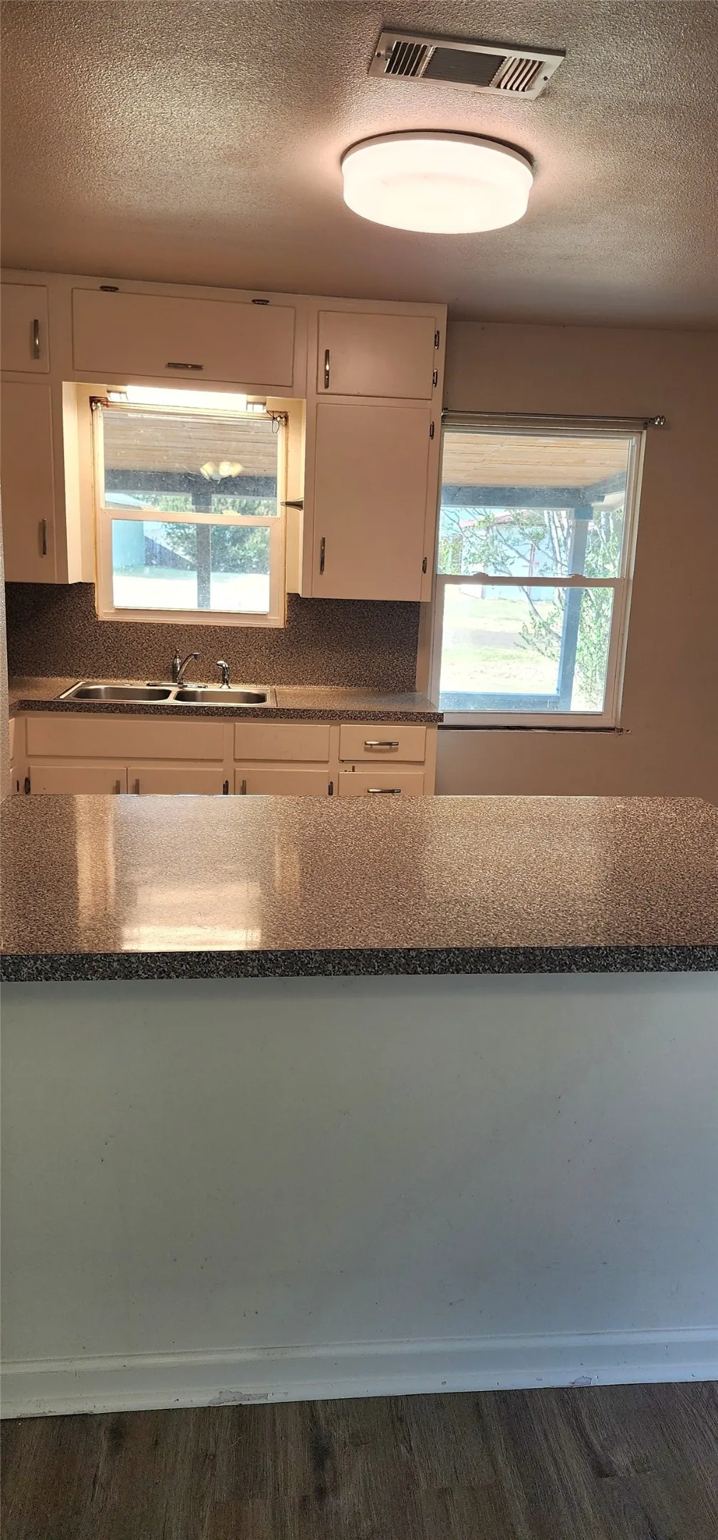 Vinyl flooring, white cabinetry, dark speckled countertops, and a double-basin sink