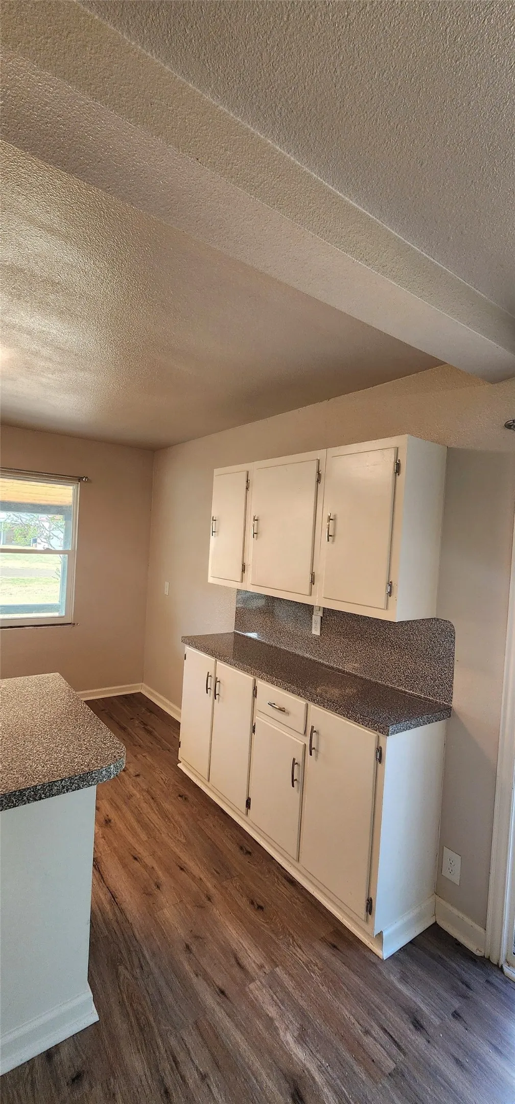 Vinyl flooring, white cabinetry, speckled countertops, and a single window