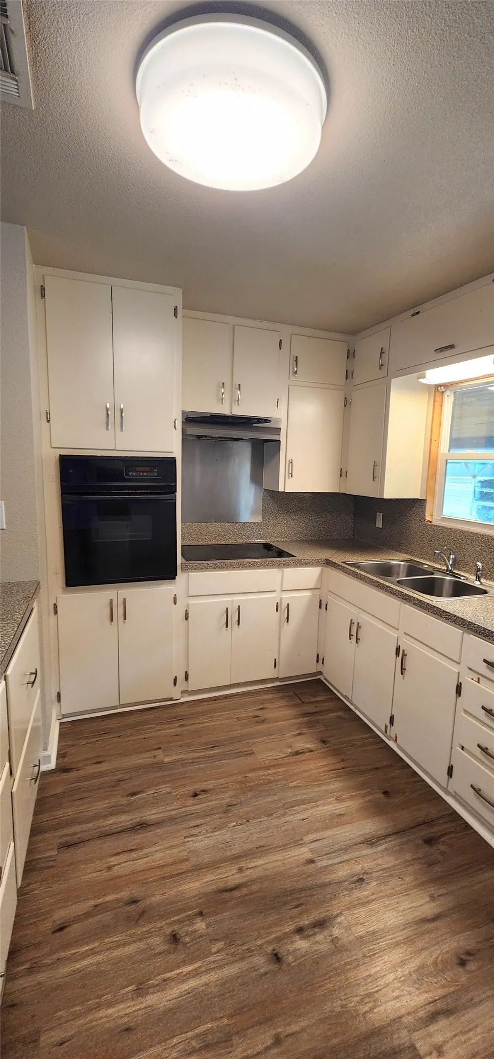Kitchen featuring white cabinetry, integrated wall oven, vinyl flooring, dual basin sink, and ample countertop space