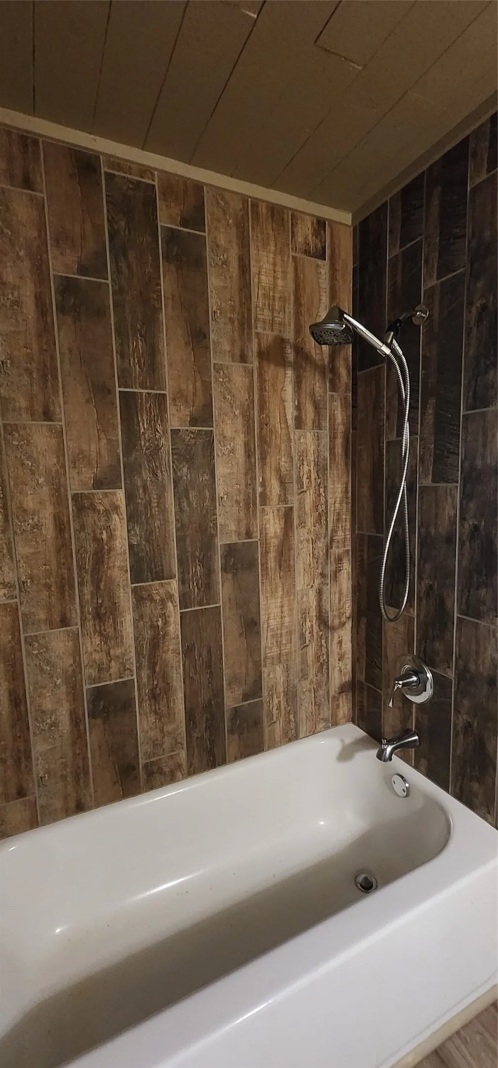 Bathtub with a chrome shower fixture, a handheld showerhead, and tile