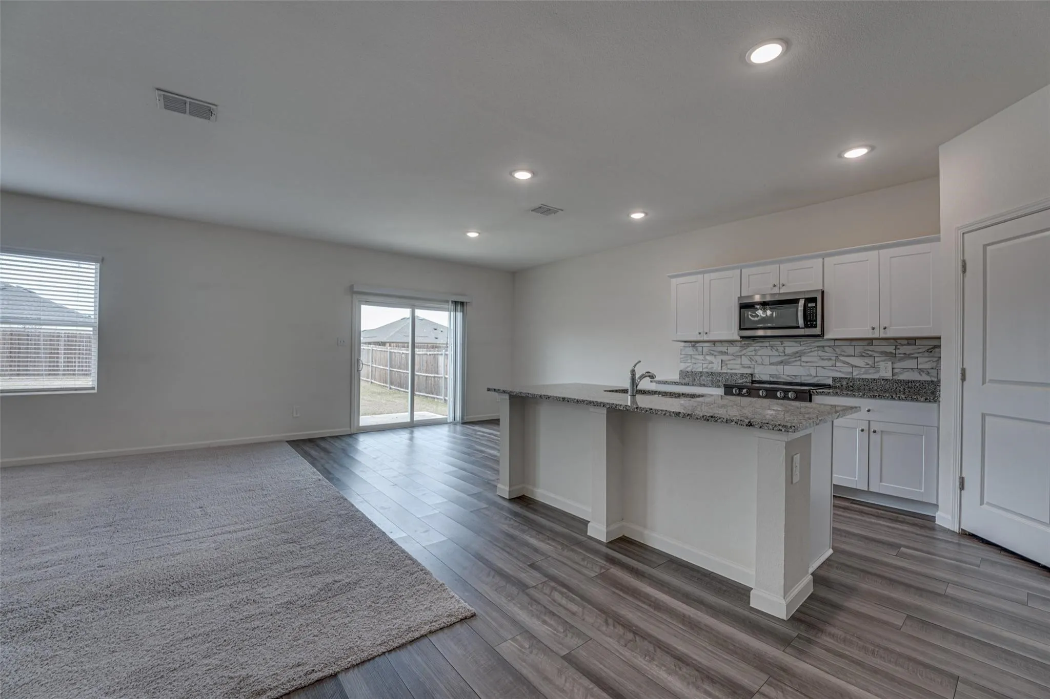 Recessed lighting, wood-finish flooring, white cabinetry, integrated microwave, and a sliding glass door