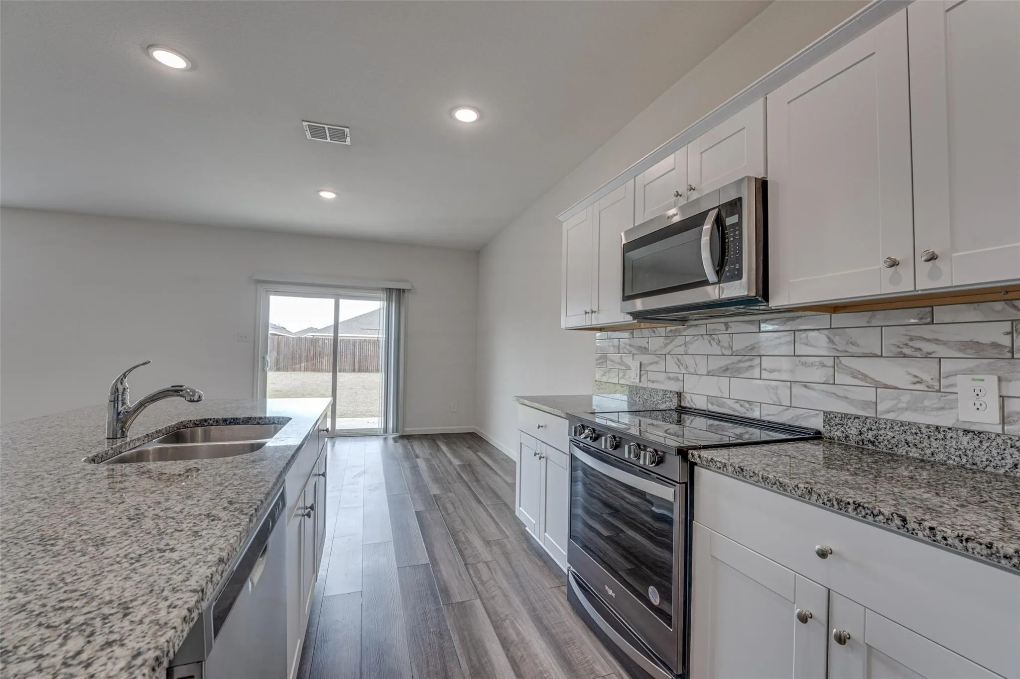 Kitchen featuring granite countertops, a stainless steel oven with a glass cooktop, a stainless steel microwave, white cabinetry, and wood-finish flooring