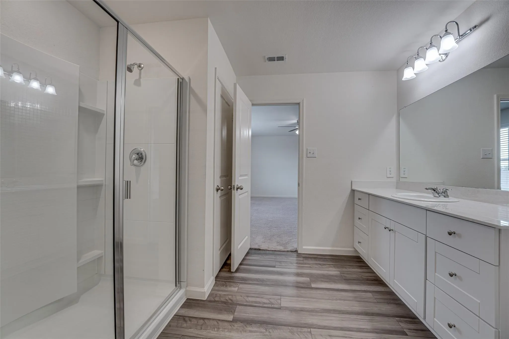 Glass-enclosed shower with subway tile surround, double vanity with quartz-finish countertop, and wood-finish flooring